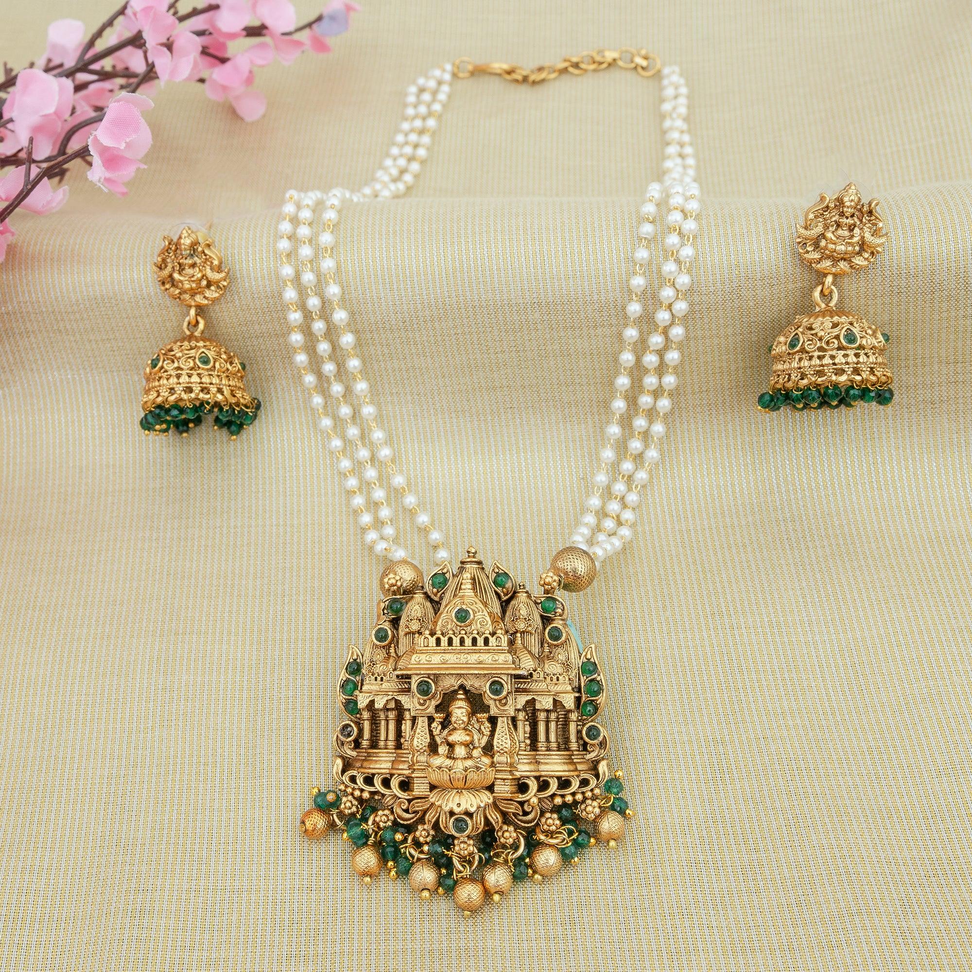 Gold necklace with green gemstones and matching earrings on a beige fabric background