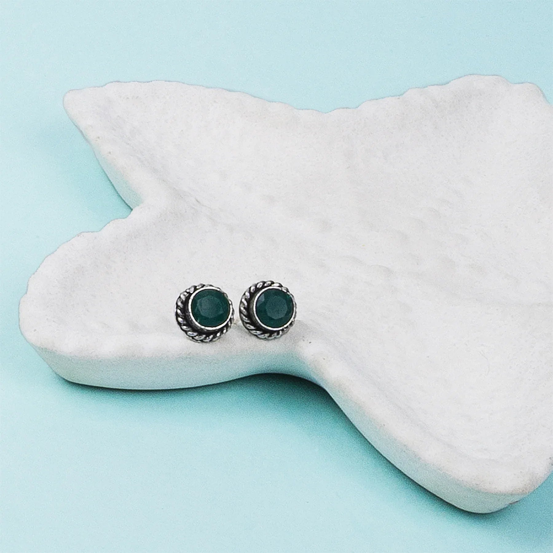 Pair of green gemstone stud earrings on a white jewelry display.