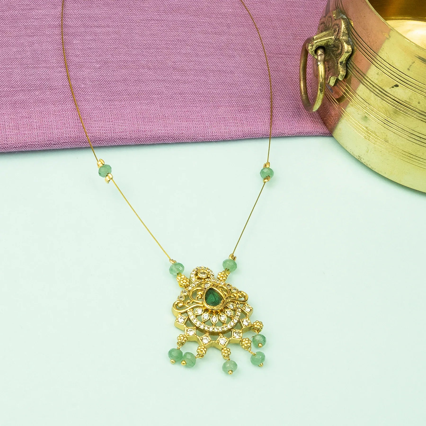 Gold necklace with green beads on a light green background