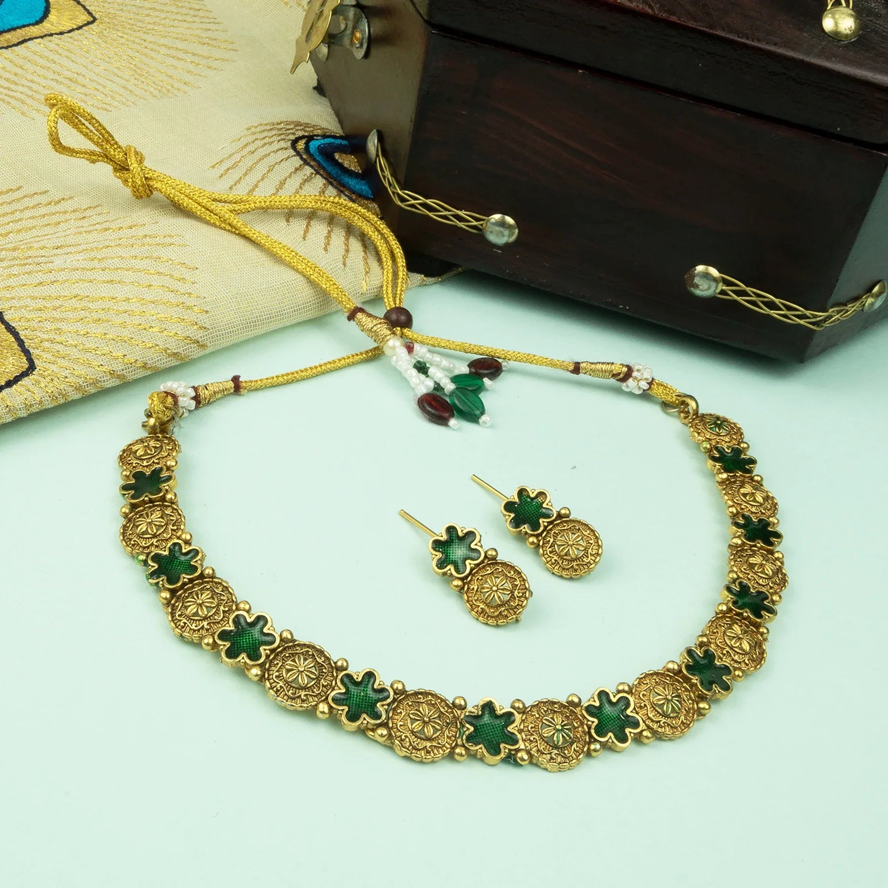 Gold necklace with green stones and matching earrings on a light green surface.