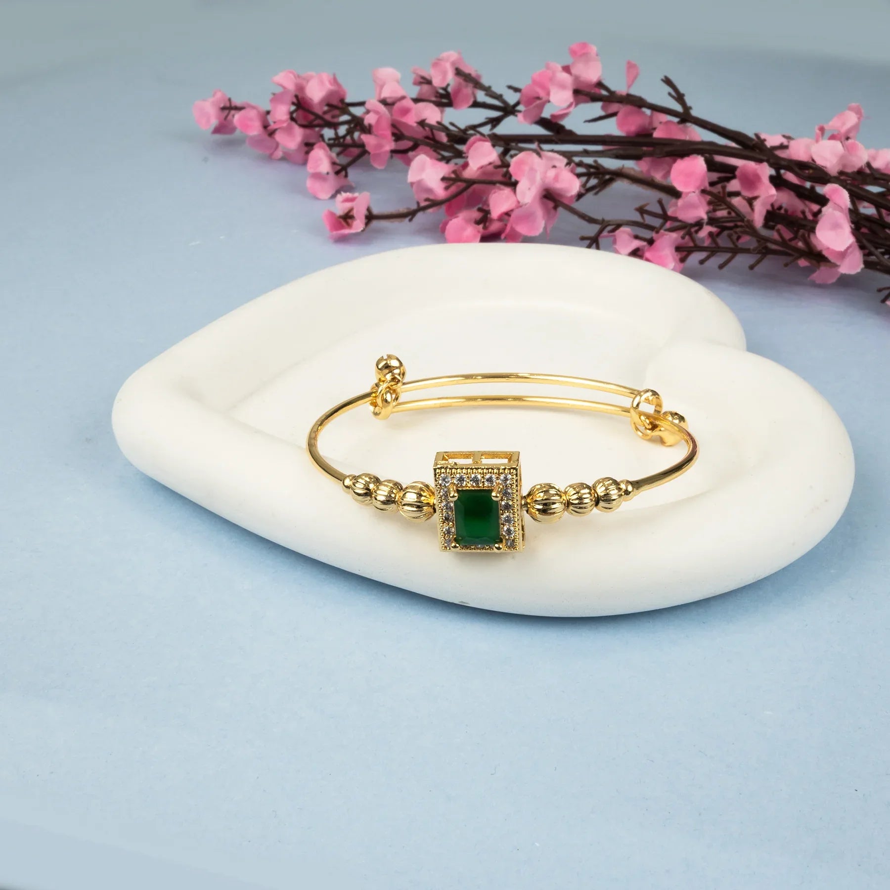 Gold bracelet with a green gemstone on a white stone with pink flowers in the background