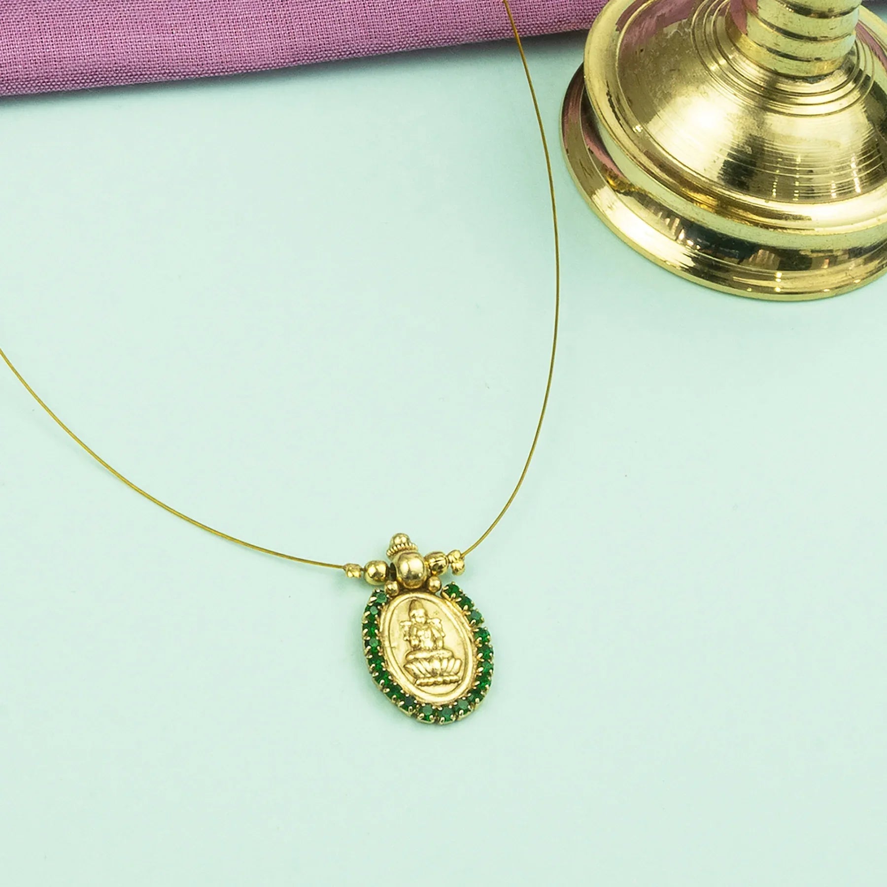 Gold necklace with a green pendant on a light green background