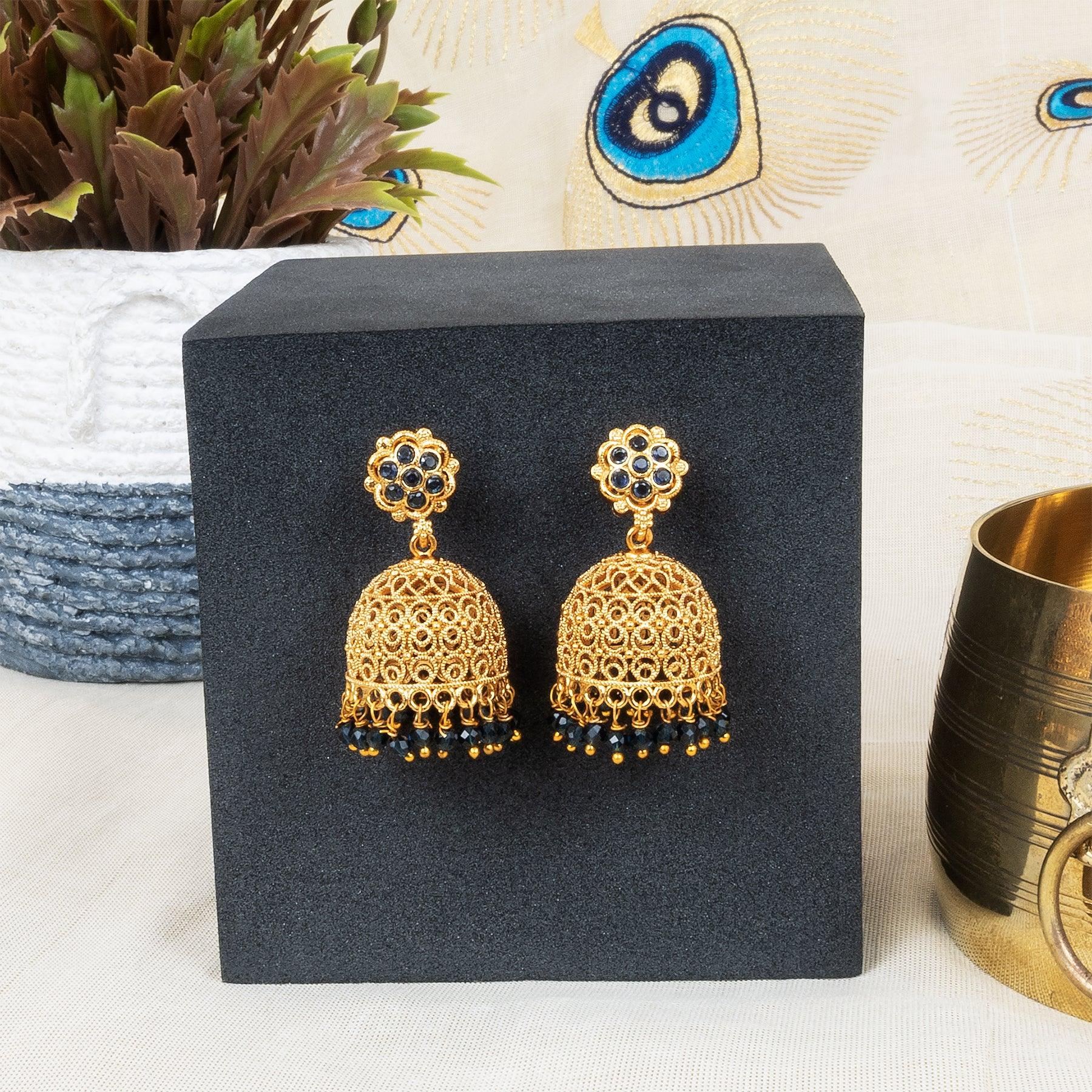 Gold earrings on a black stand with a decorative background