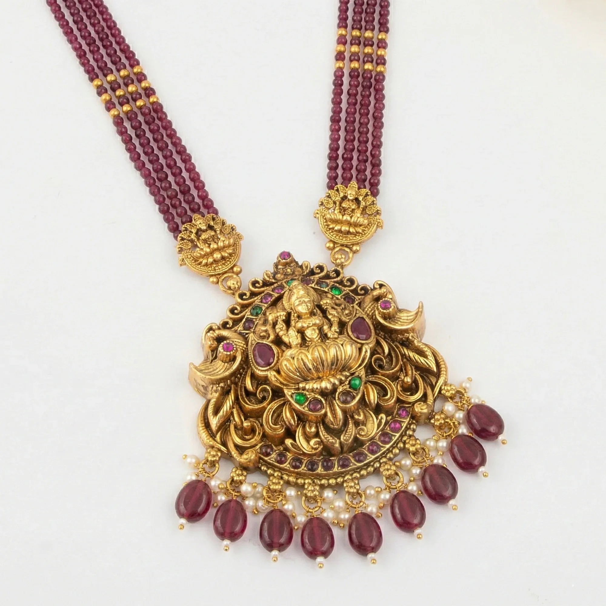 Gold necklace with maroon beads and intricate design on a white background