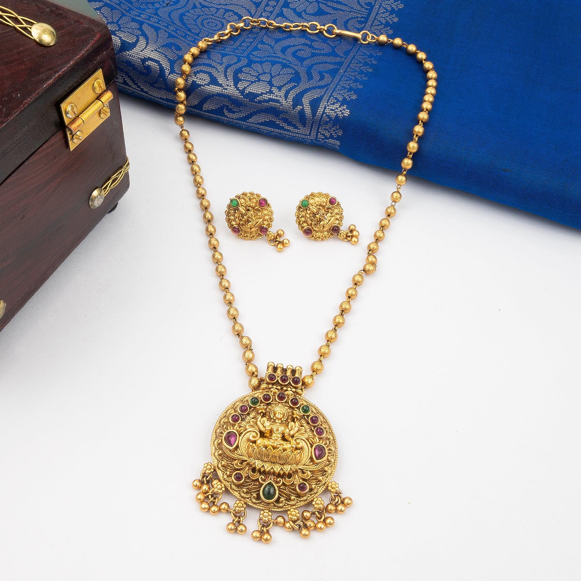 Gold necklace with pendant and matching earrings on a white surface with a blue fabric and wooden box in the background.