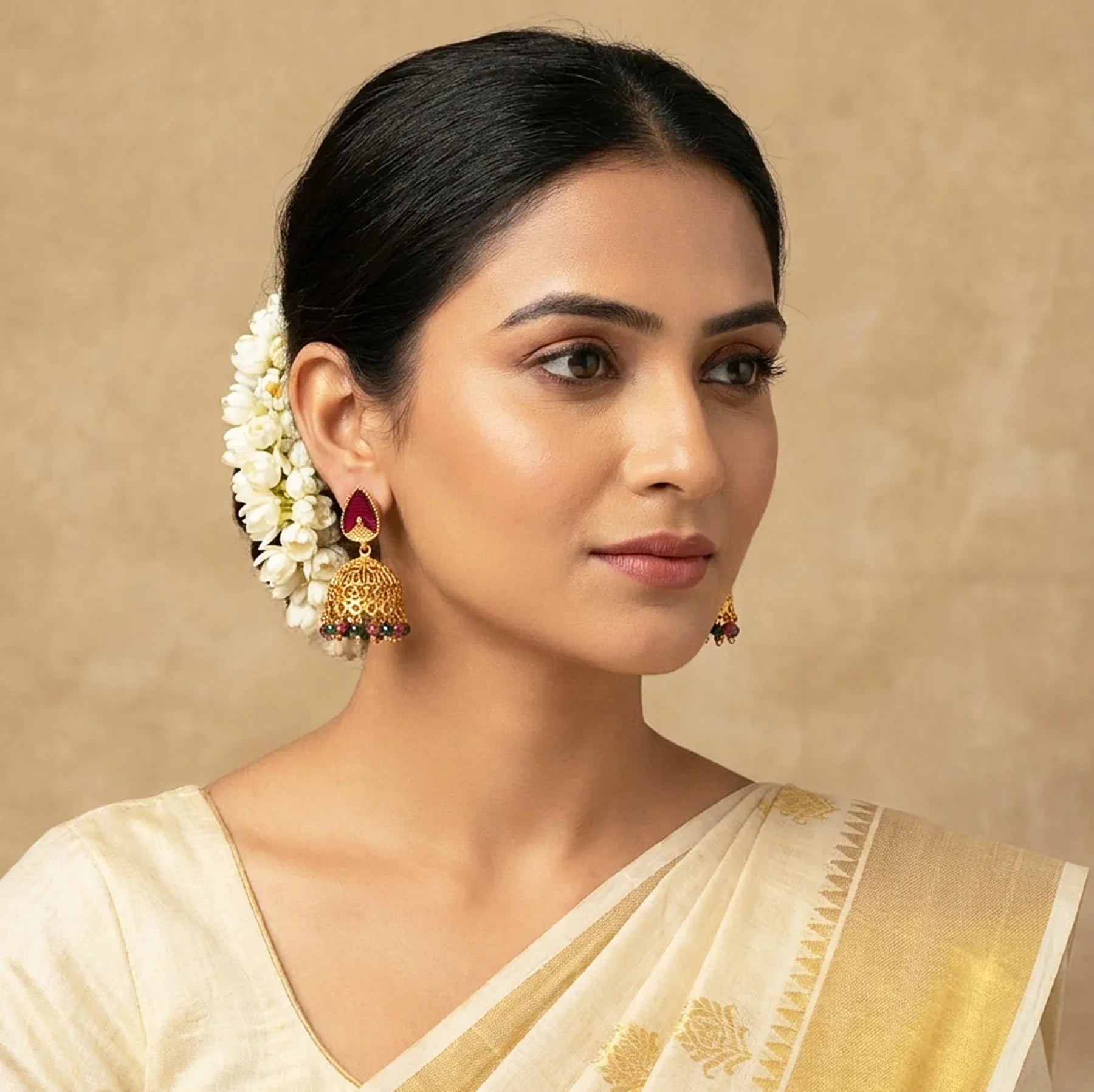 Woman wearing a cream saree with gold border and white floral earrings against a beige background