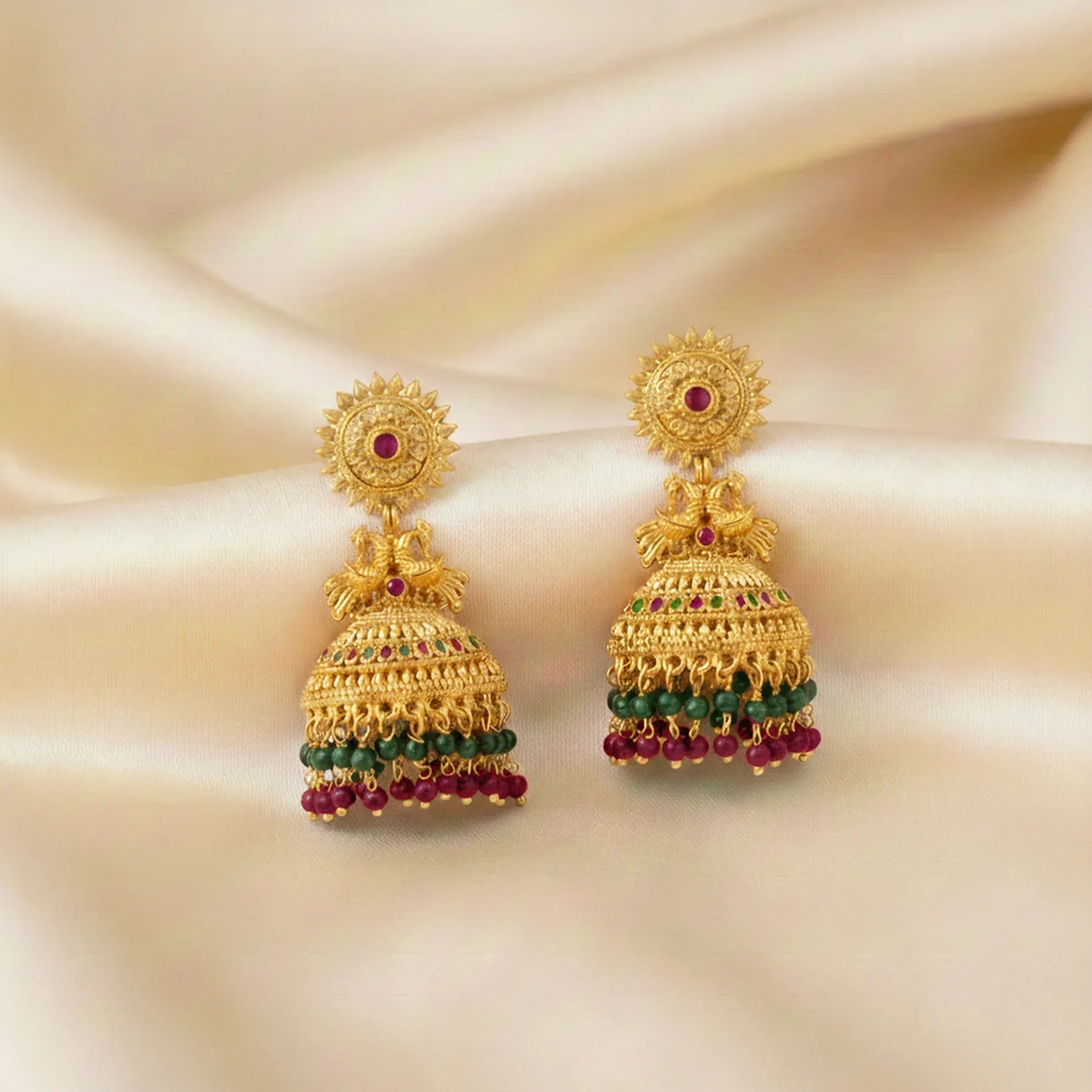 Gold earrings with gemstones on a beige fabric background