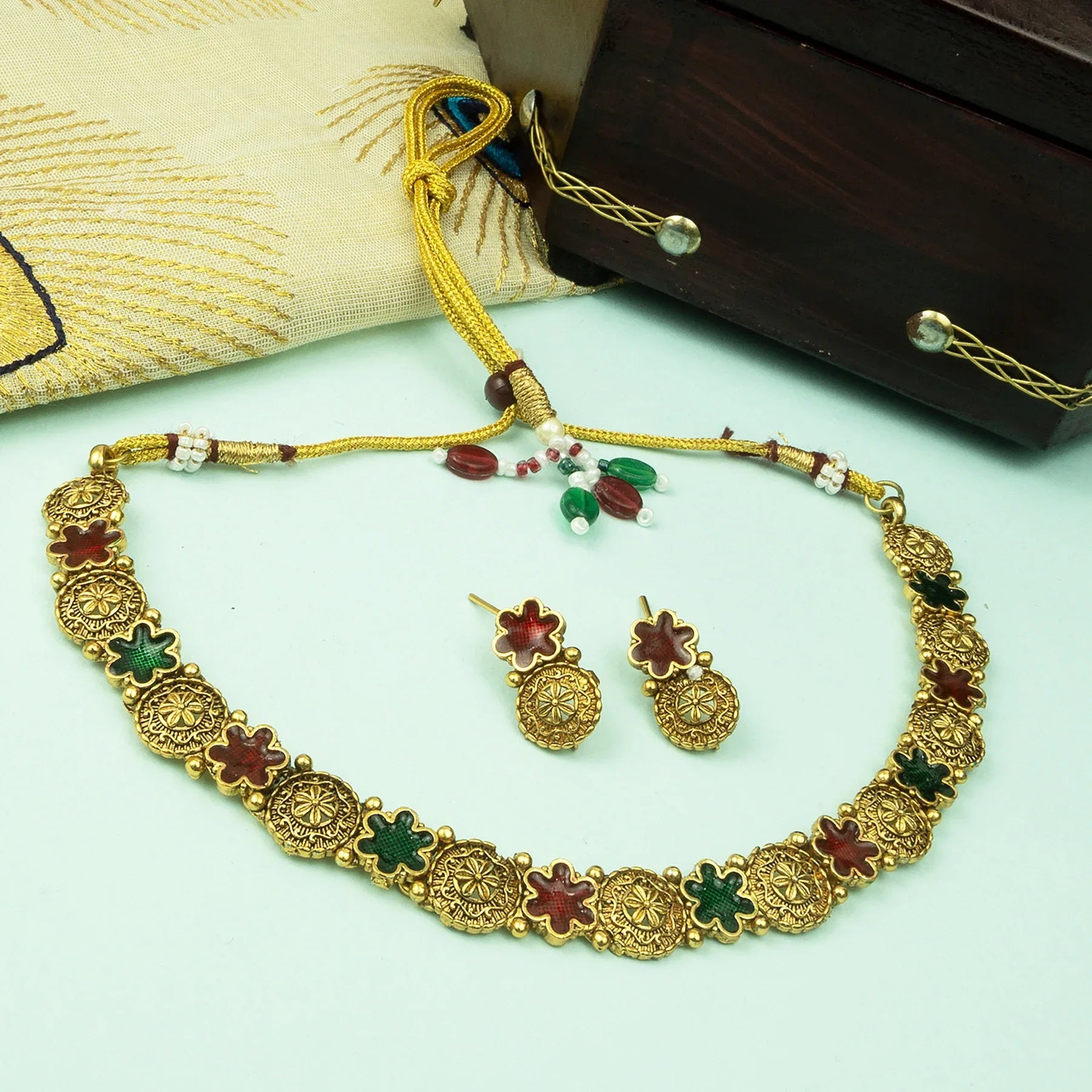 Gold necklace with colorful stones and matching earrings on a light green surface.