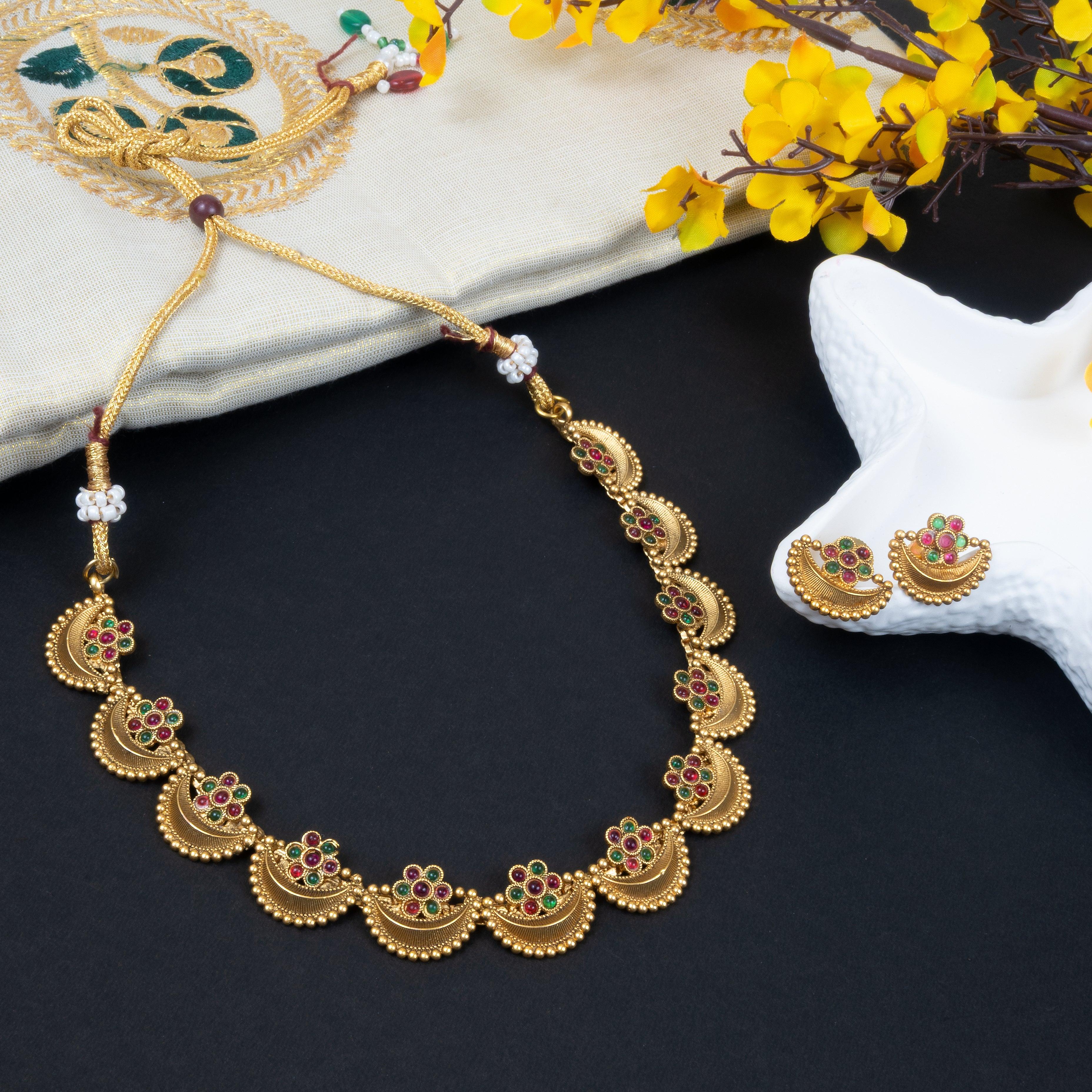Gold necklace with floral designs on a dark surface with yellow flowers and a white starfish.