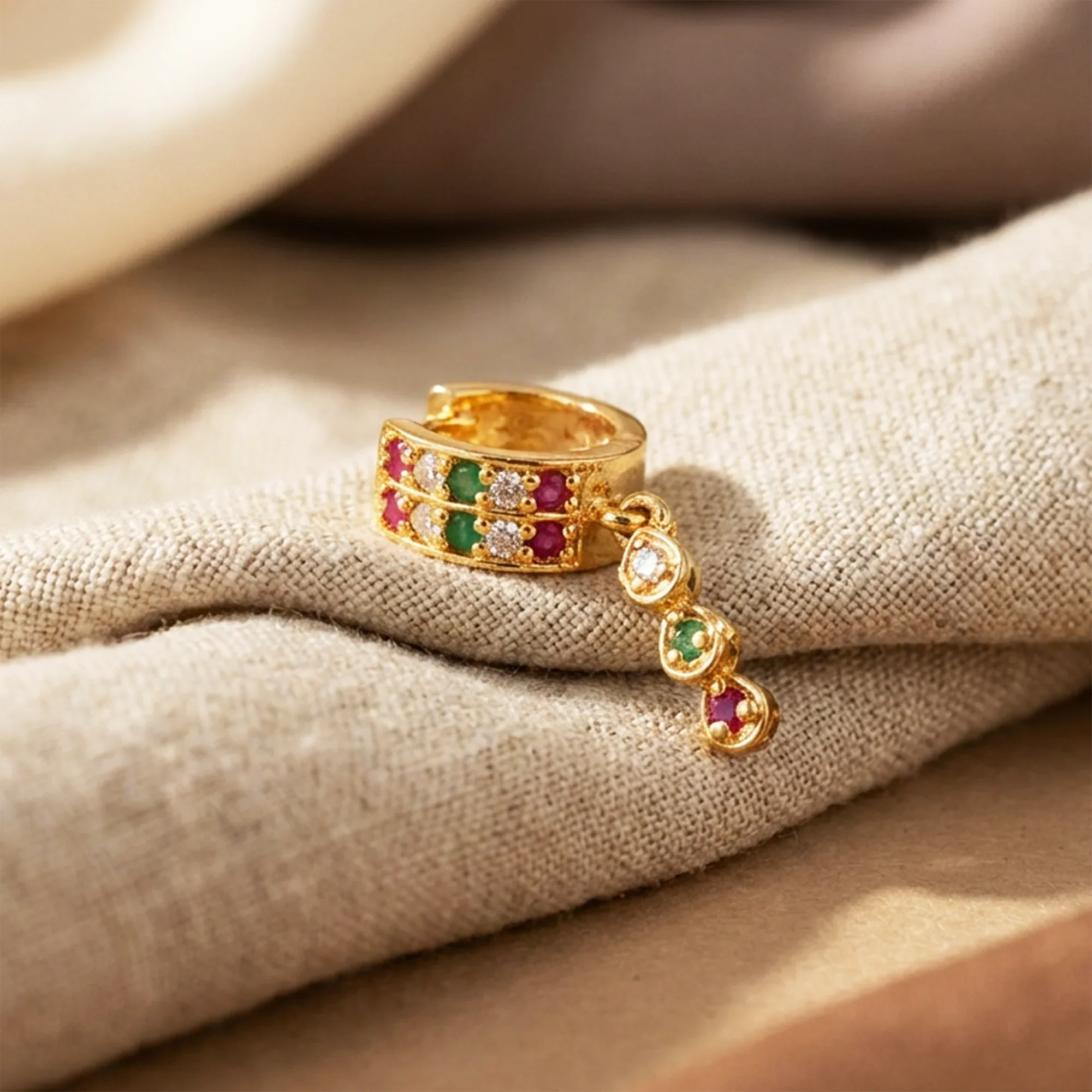 Gold ring with colorful gemstones on a beige fabric background