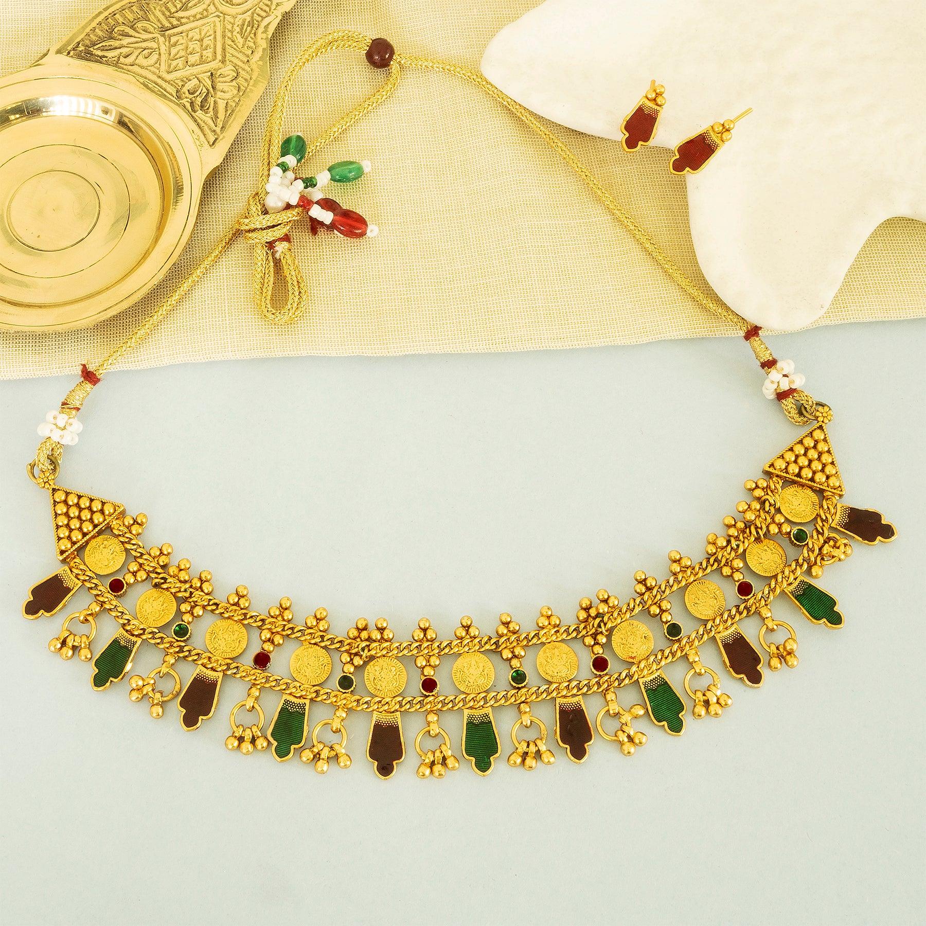 Gold necklace with green and red stones on a light gray background