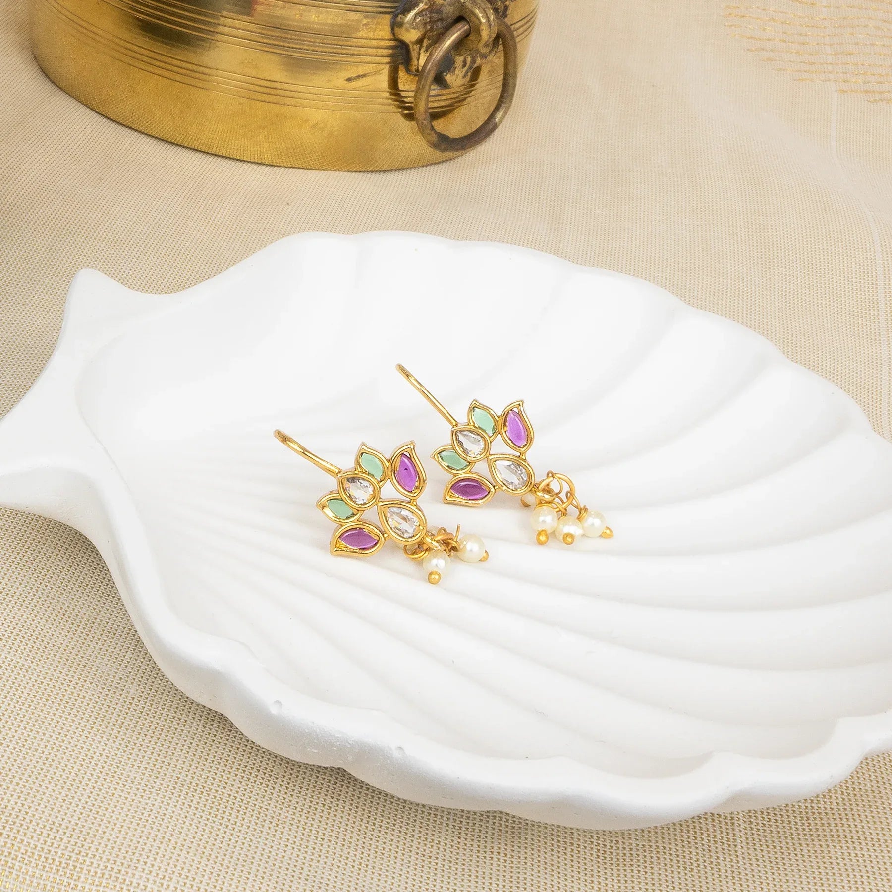 Gold earrings with colorful stones on a white dish, with a gold box in the background.