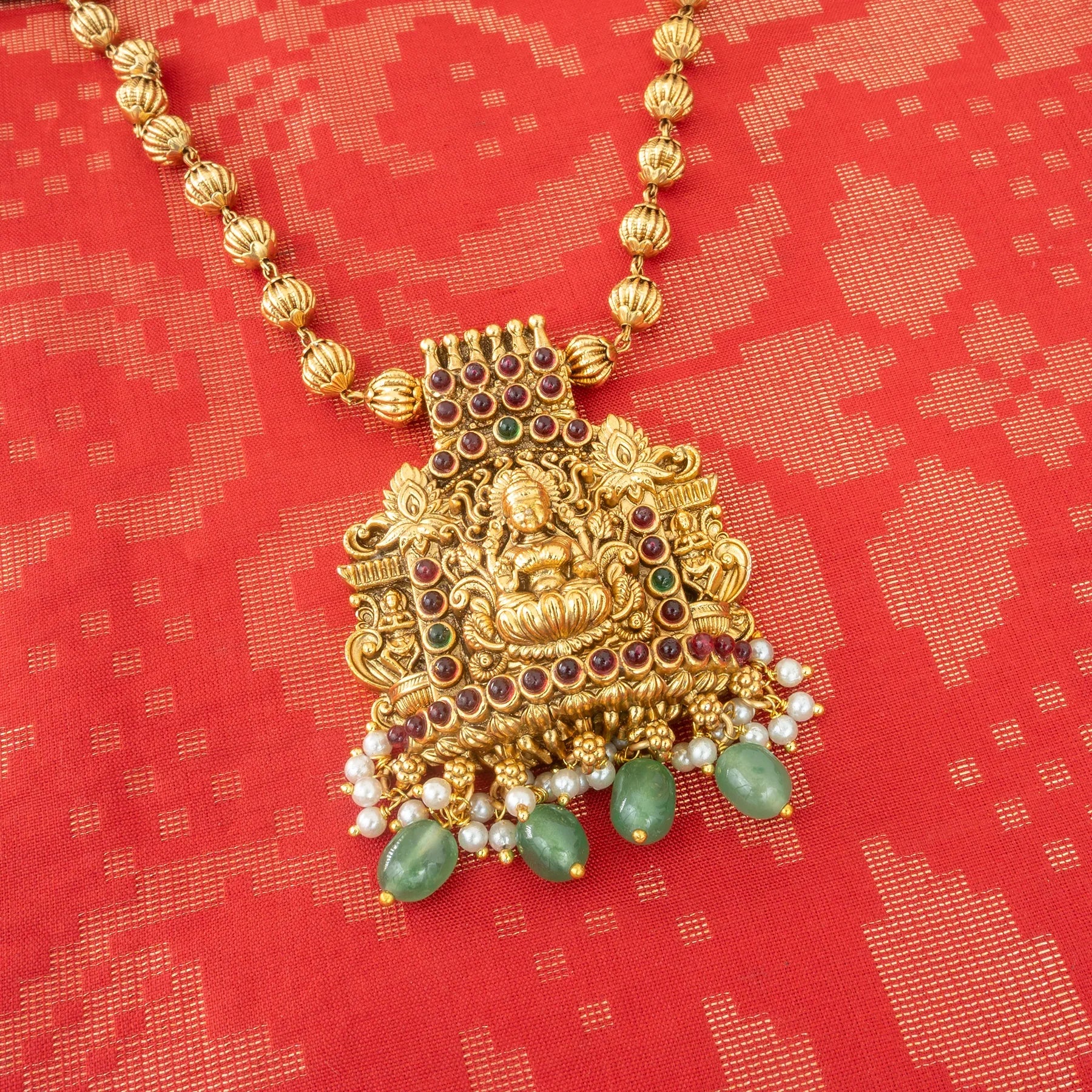 Gold necklace with a pendant on a red patterned background