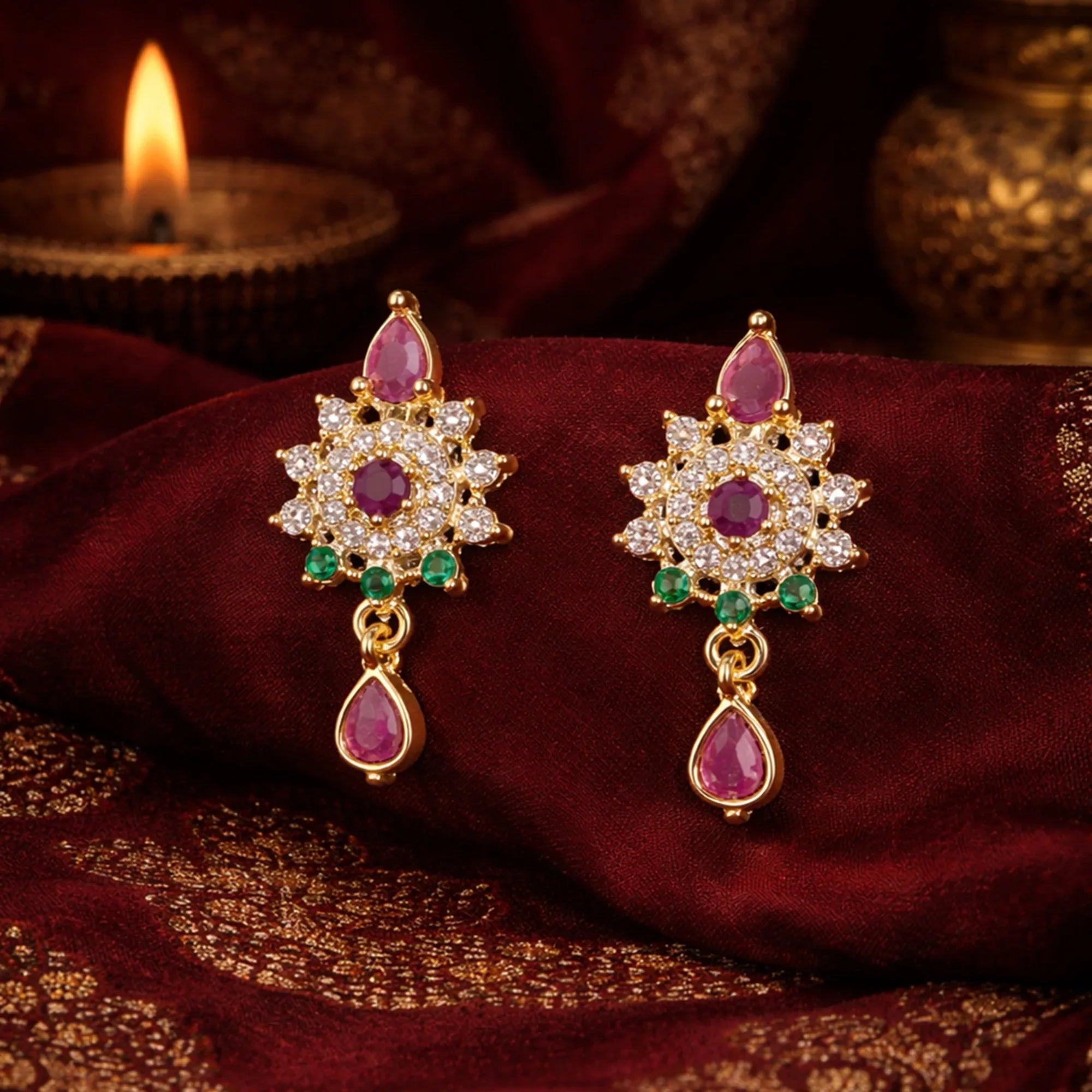 Pair of gold earrings with gemstones on a maroon fabric background