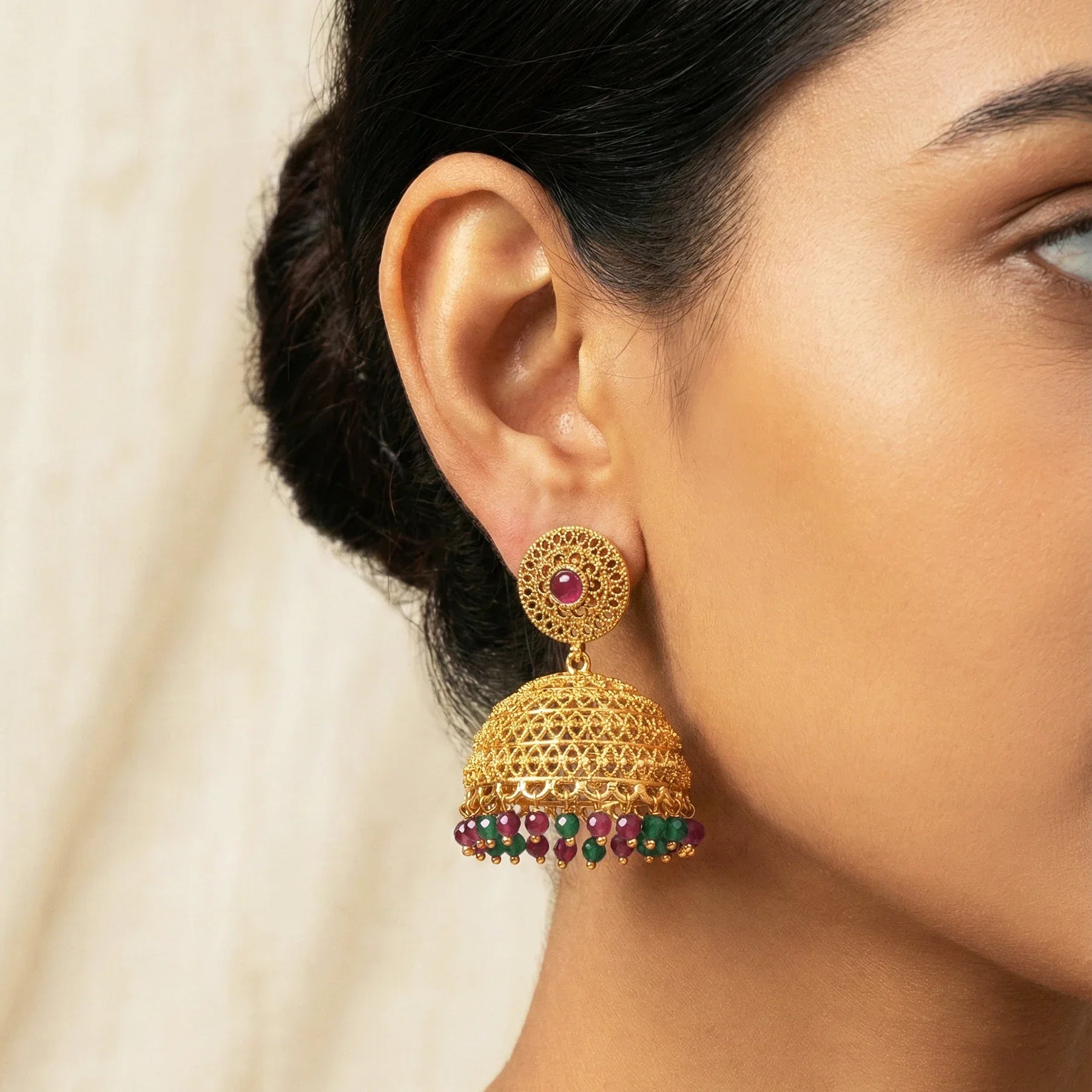 Gold earrings with red and green gemstones worn by a person