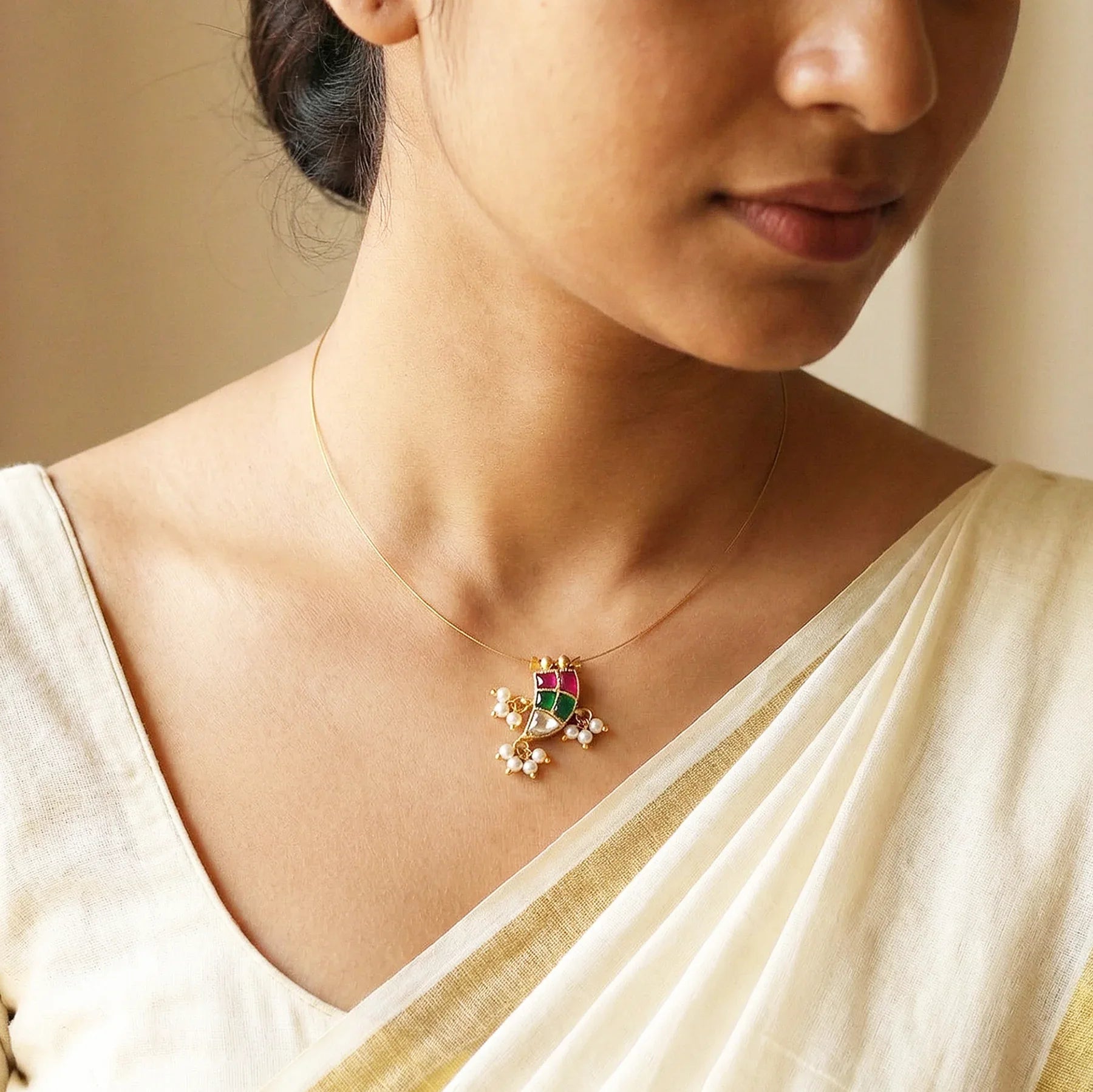 Woman wearing a gold necklace with a green and red gemstone pendant