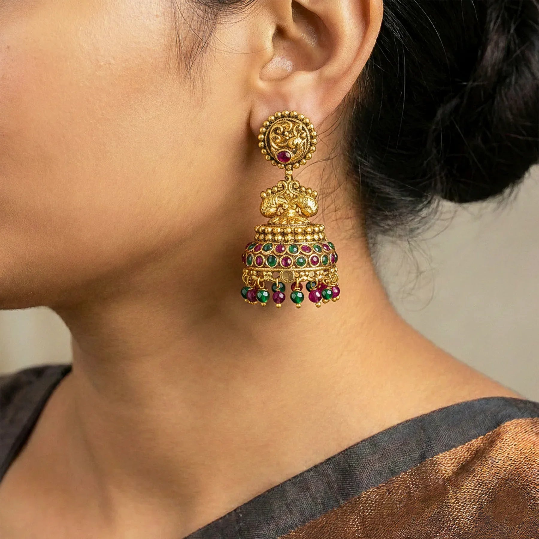 Gold earrings with green and red stones worn by a person