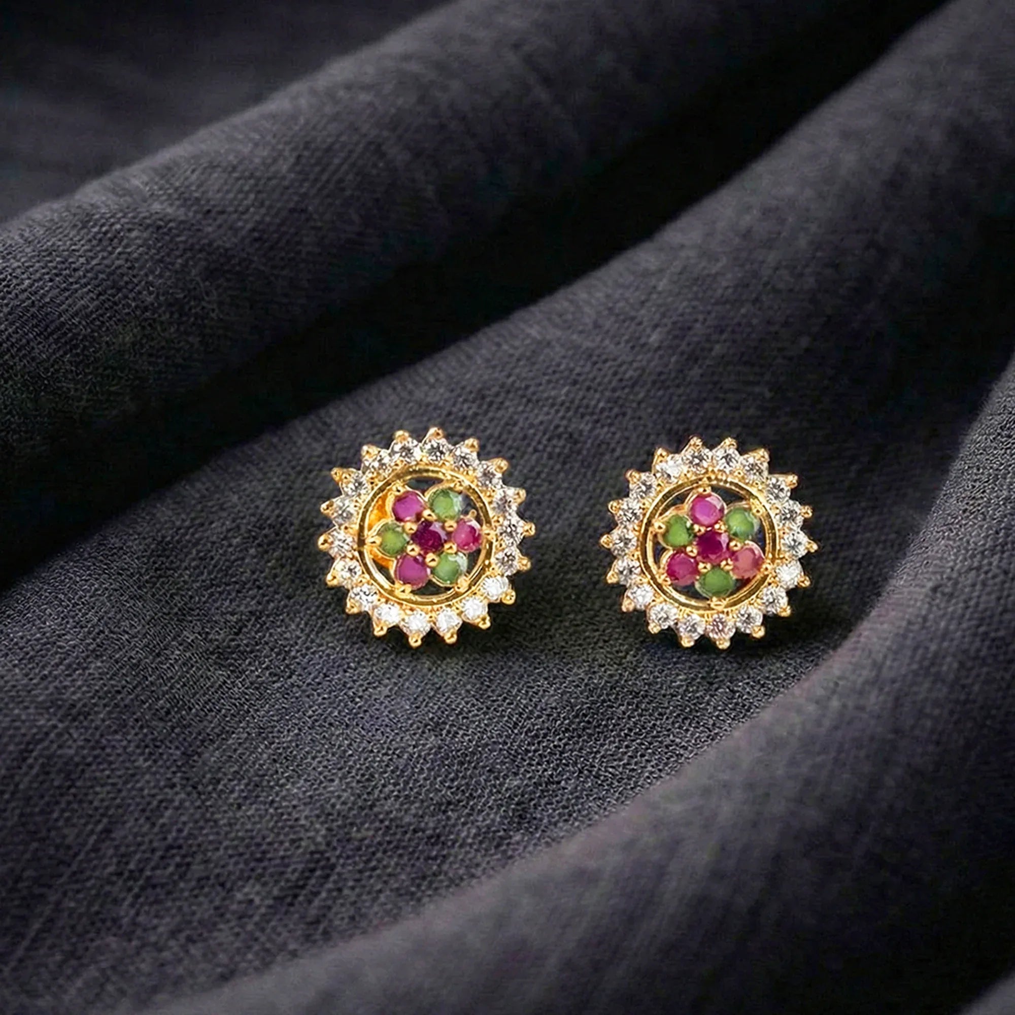 Pair of gold earrings with gemstones on a dark fabric background