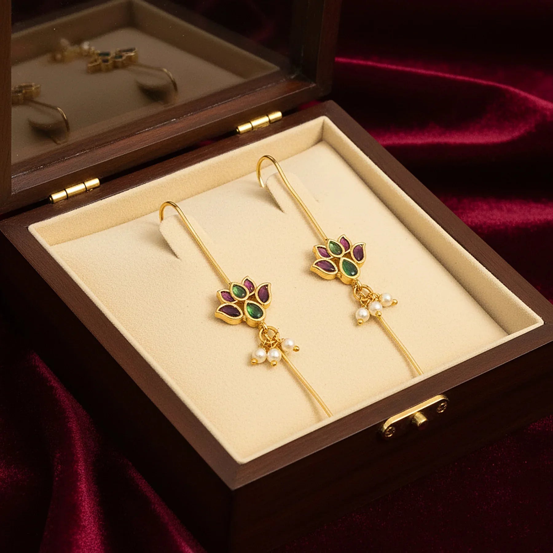 Gold earrings with gemstones in a jewelry box on a red fabric background