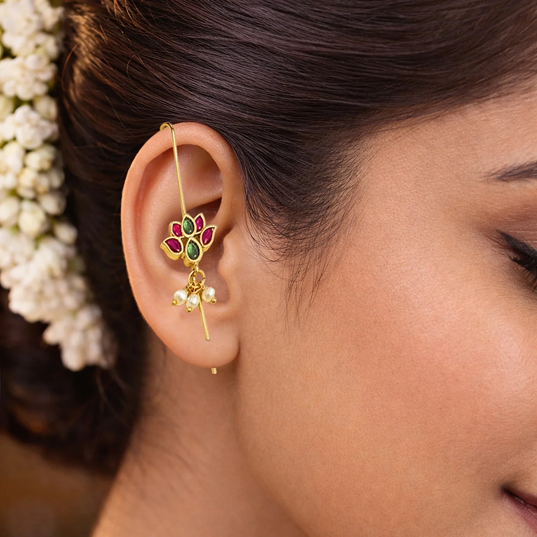 Close-up of a woman's ear wearing a gold earring with gemstones and pearls.