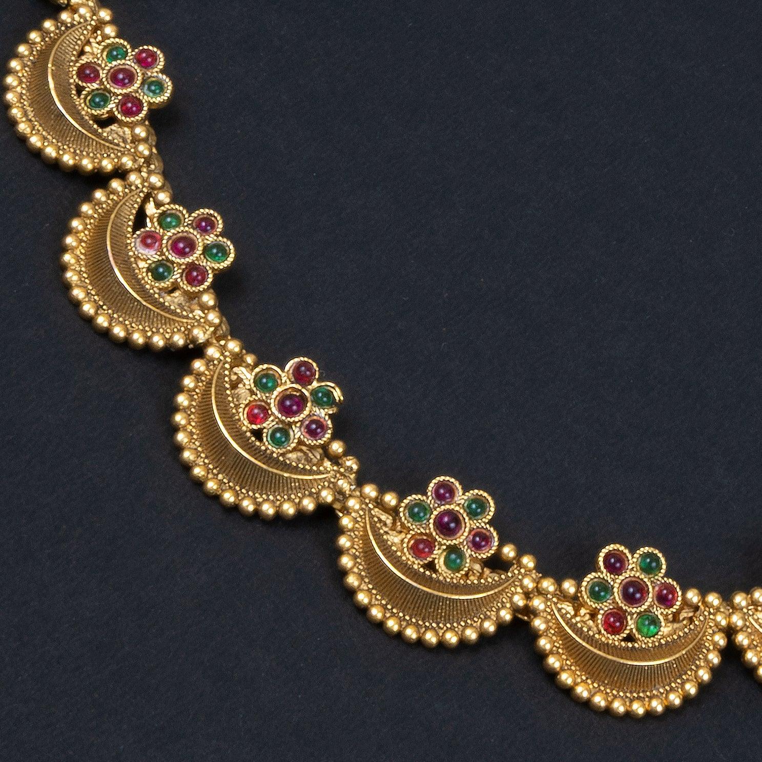 Gold necklace with floral designs and colored stones on a dark background