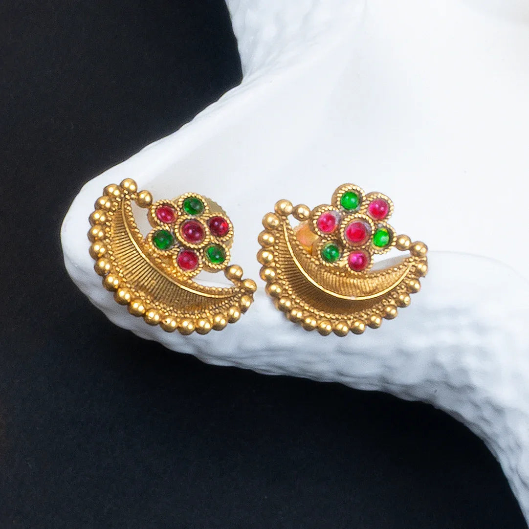 Gold earrings with red and green gemstones on a white fabric background