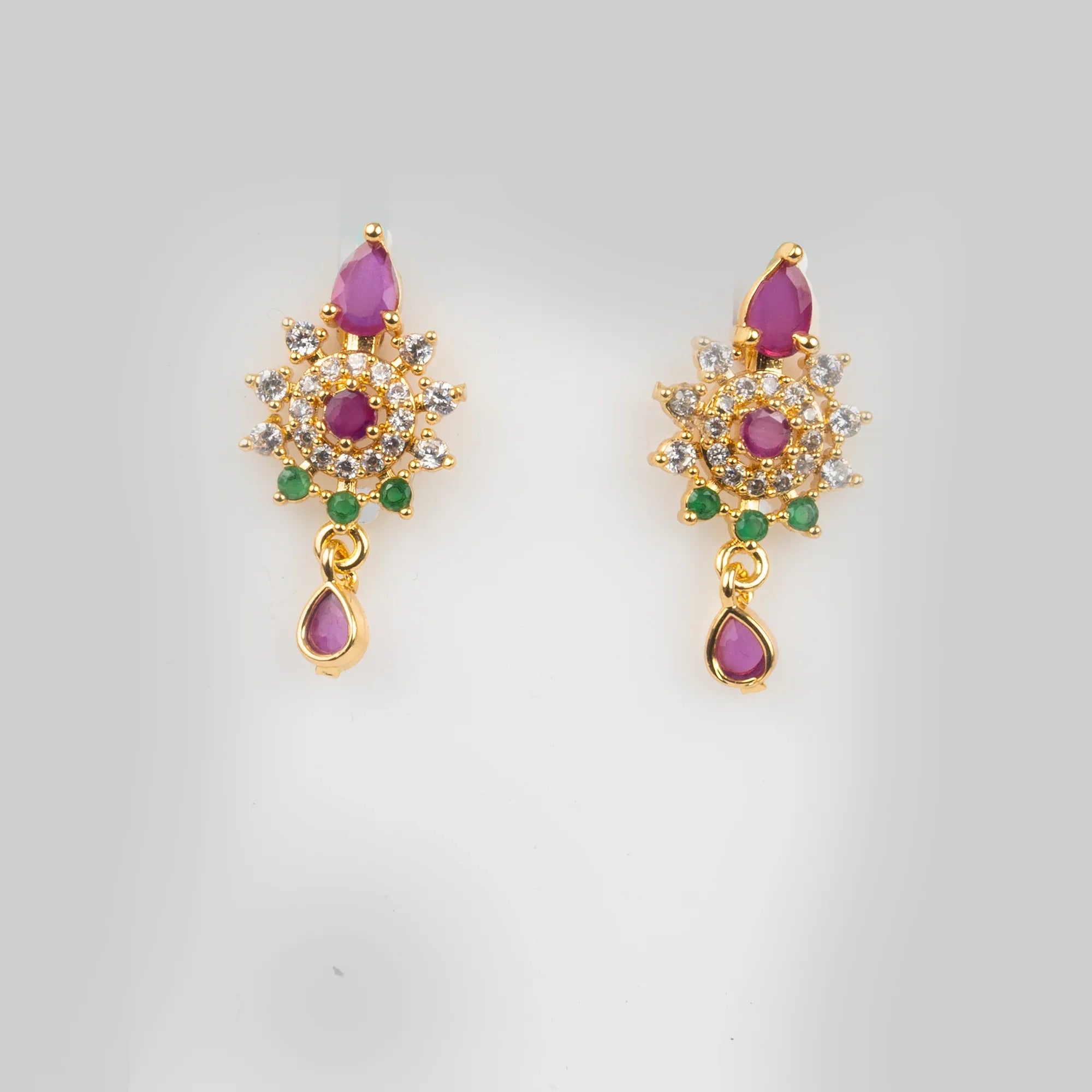 Pair of gold earrings with pink and green gemstones on a light gray background