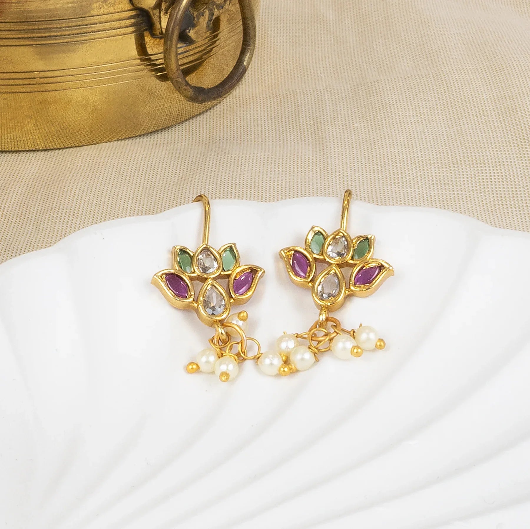 Gold earrings with gemstones and pearls on a white surface