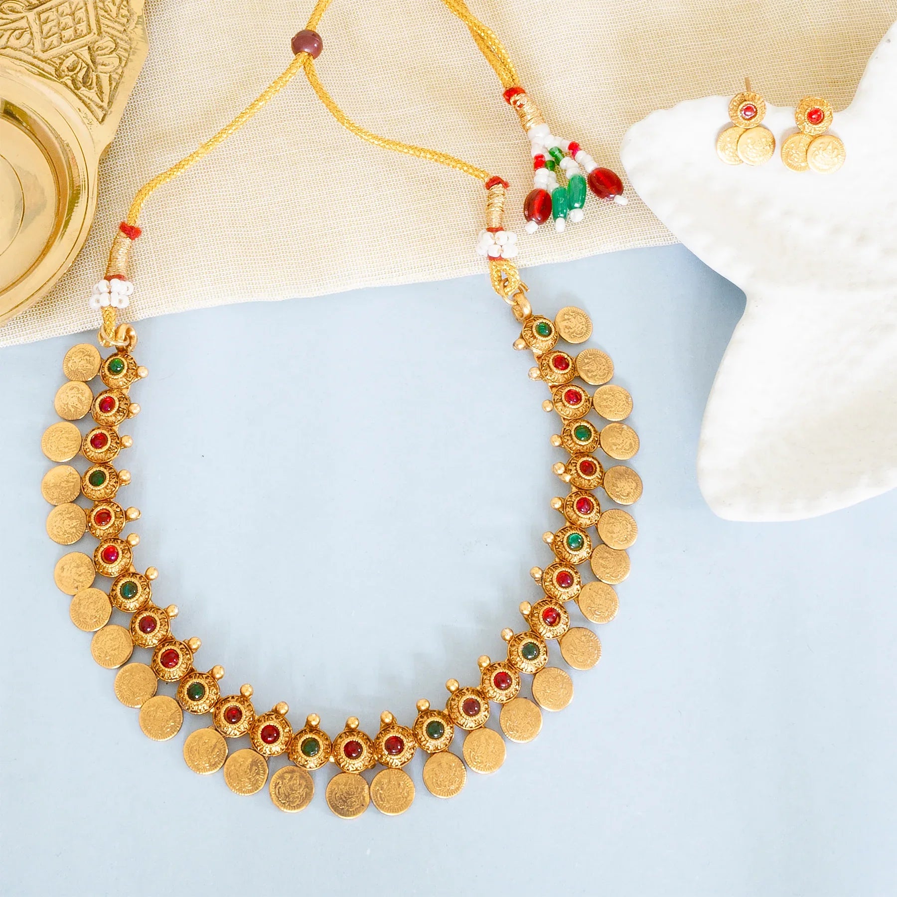 Gold necklace with red and green stones on a light blue surface