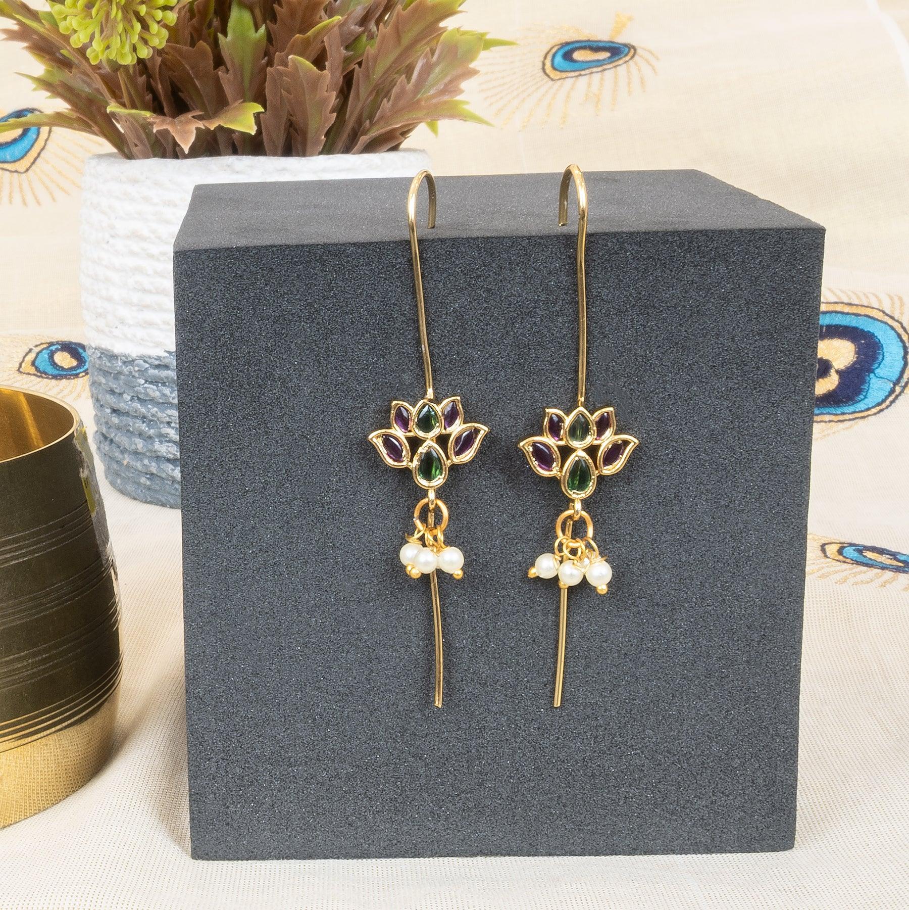 Gold lotus earrings with gemstones and pearls on a gray stand with a decorative background.