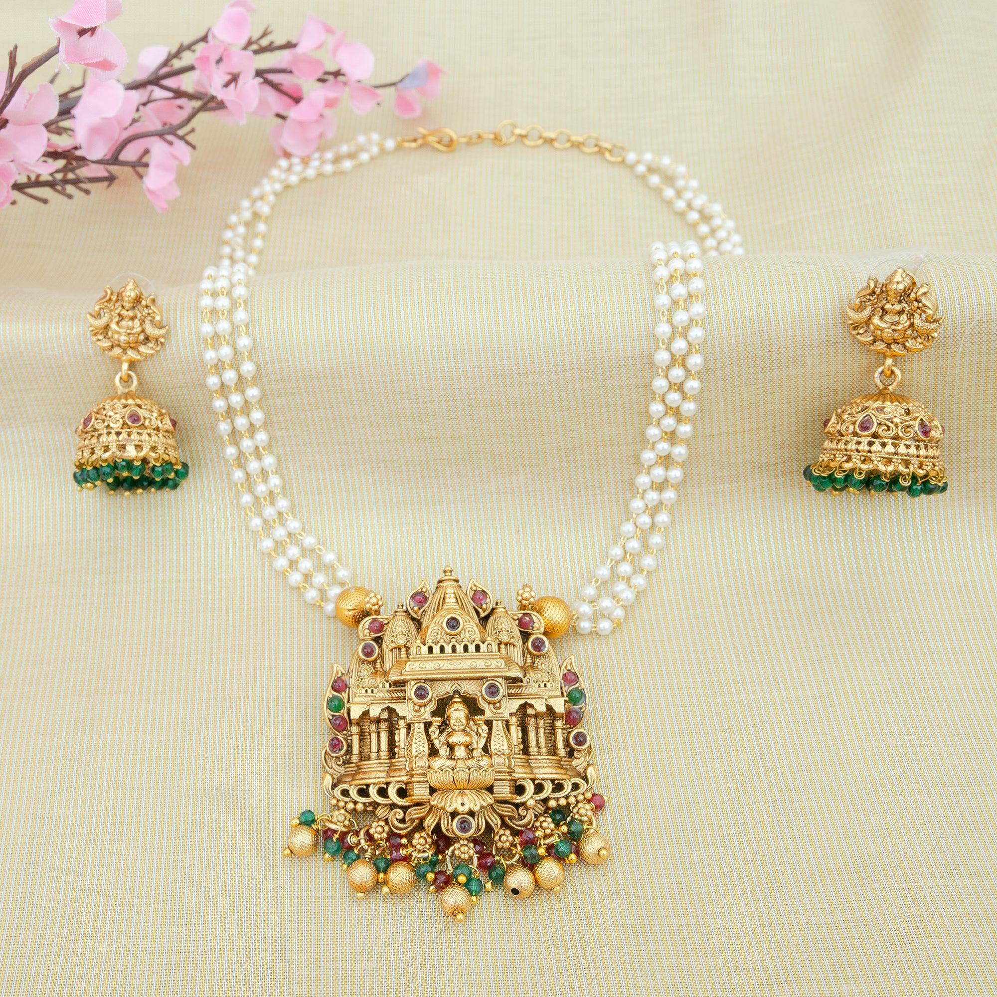 Gold necklace with temple design and matching earrings on a beige background