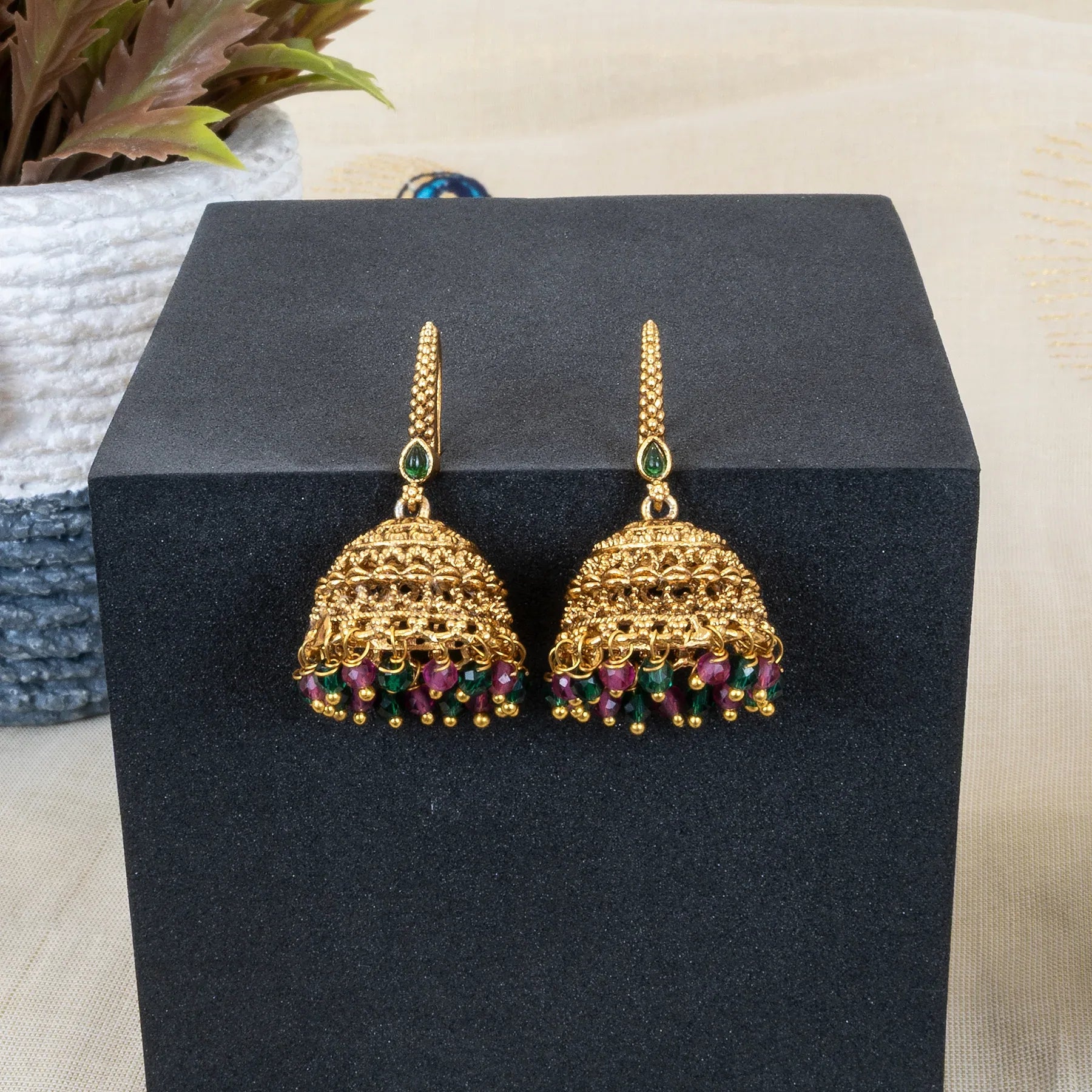 Gold earrings with green and red stones on a black box