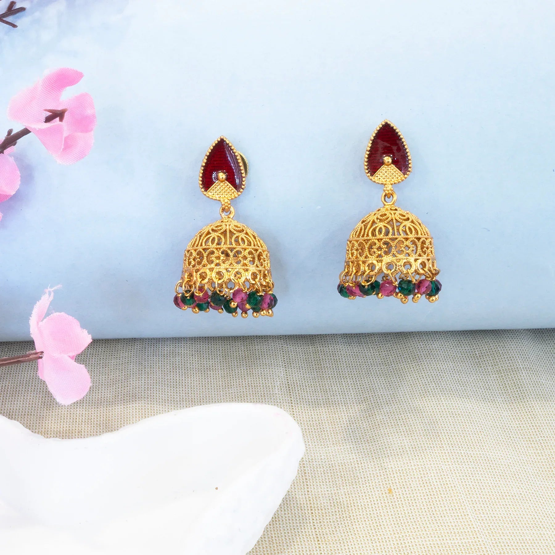 Gold earrings with red and green stones on a light blue fabric background