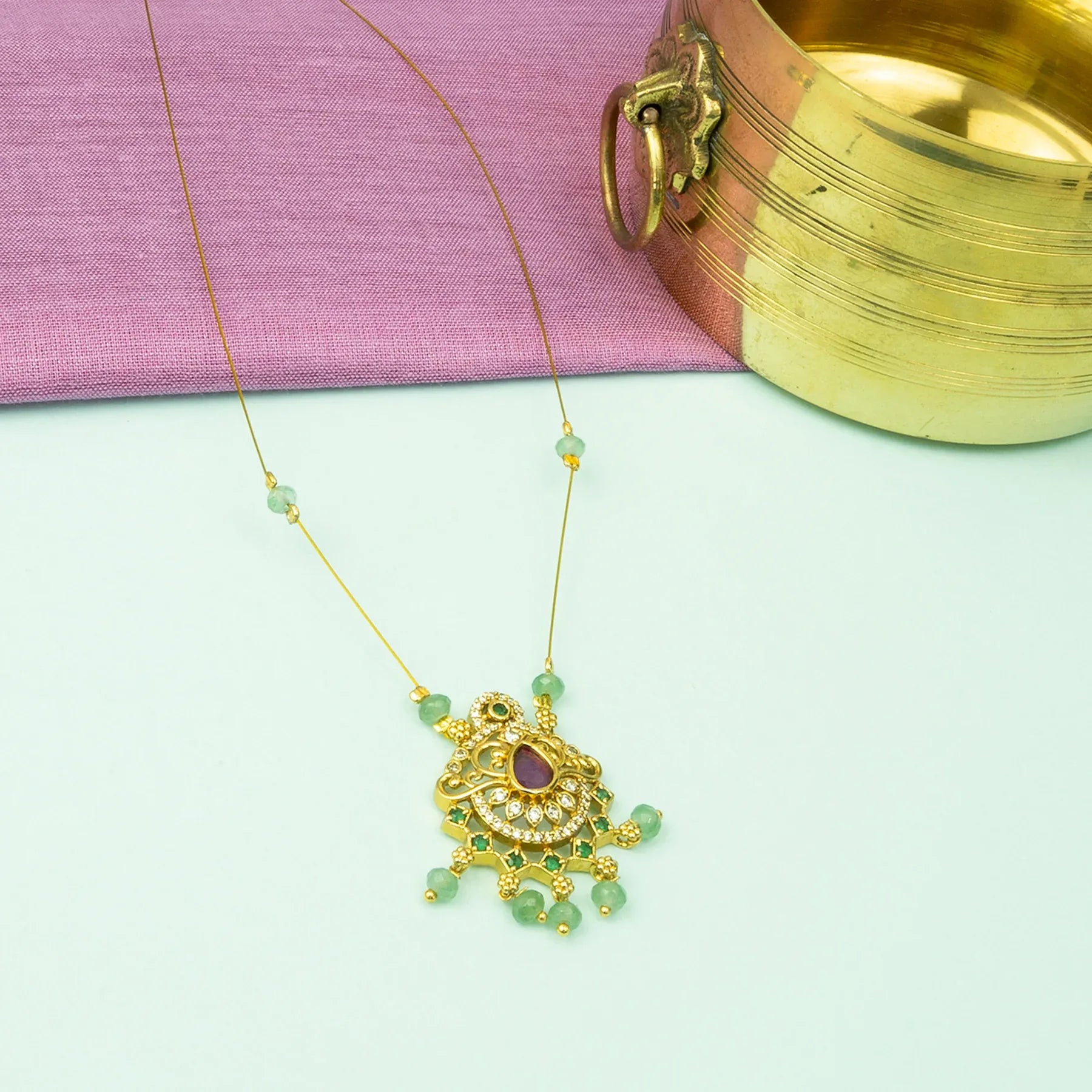 Gold necklace with green beads and a purple gemstone pendant on a light green background