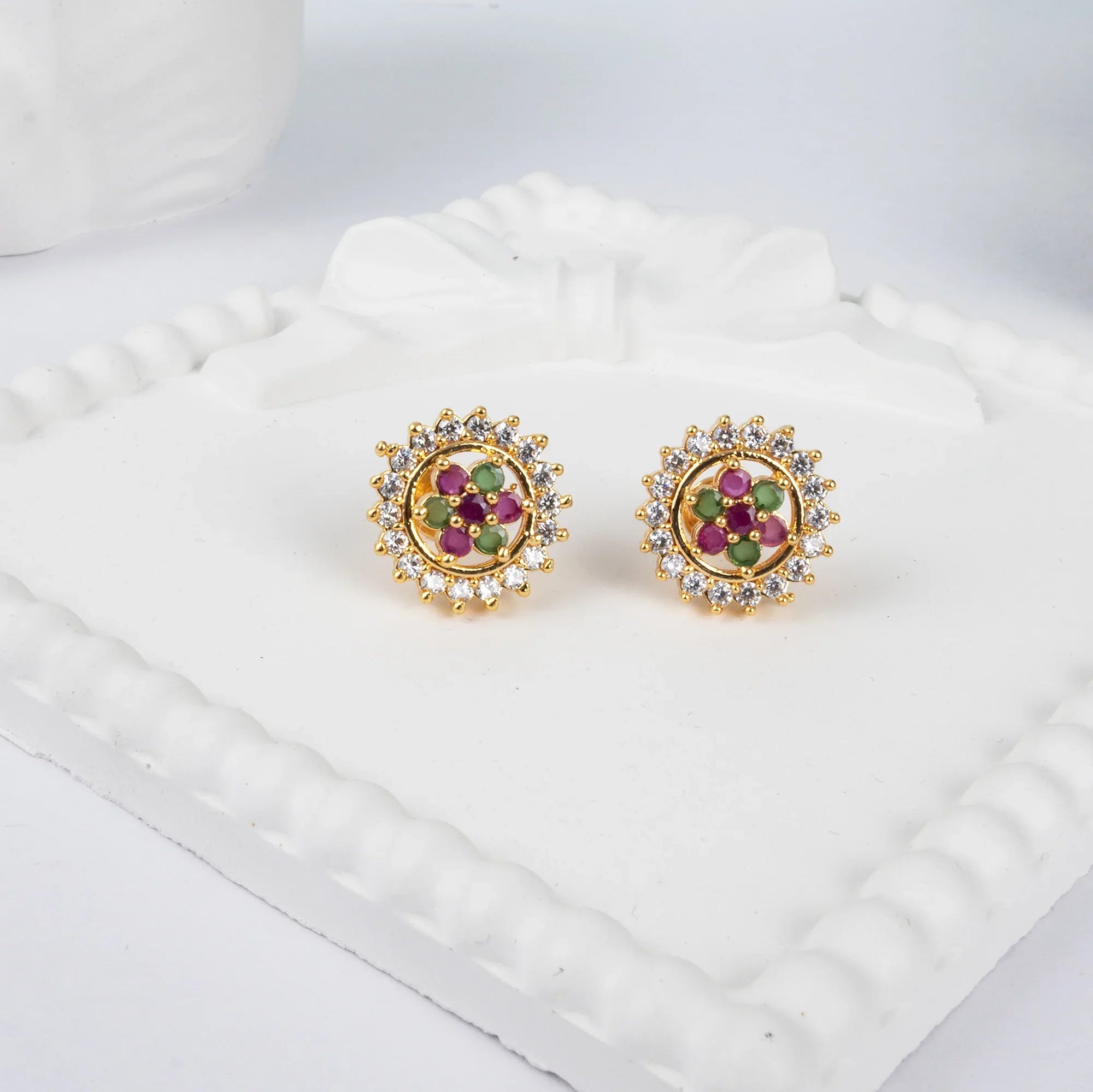 Gold earrings with gemstones on a white cushion