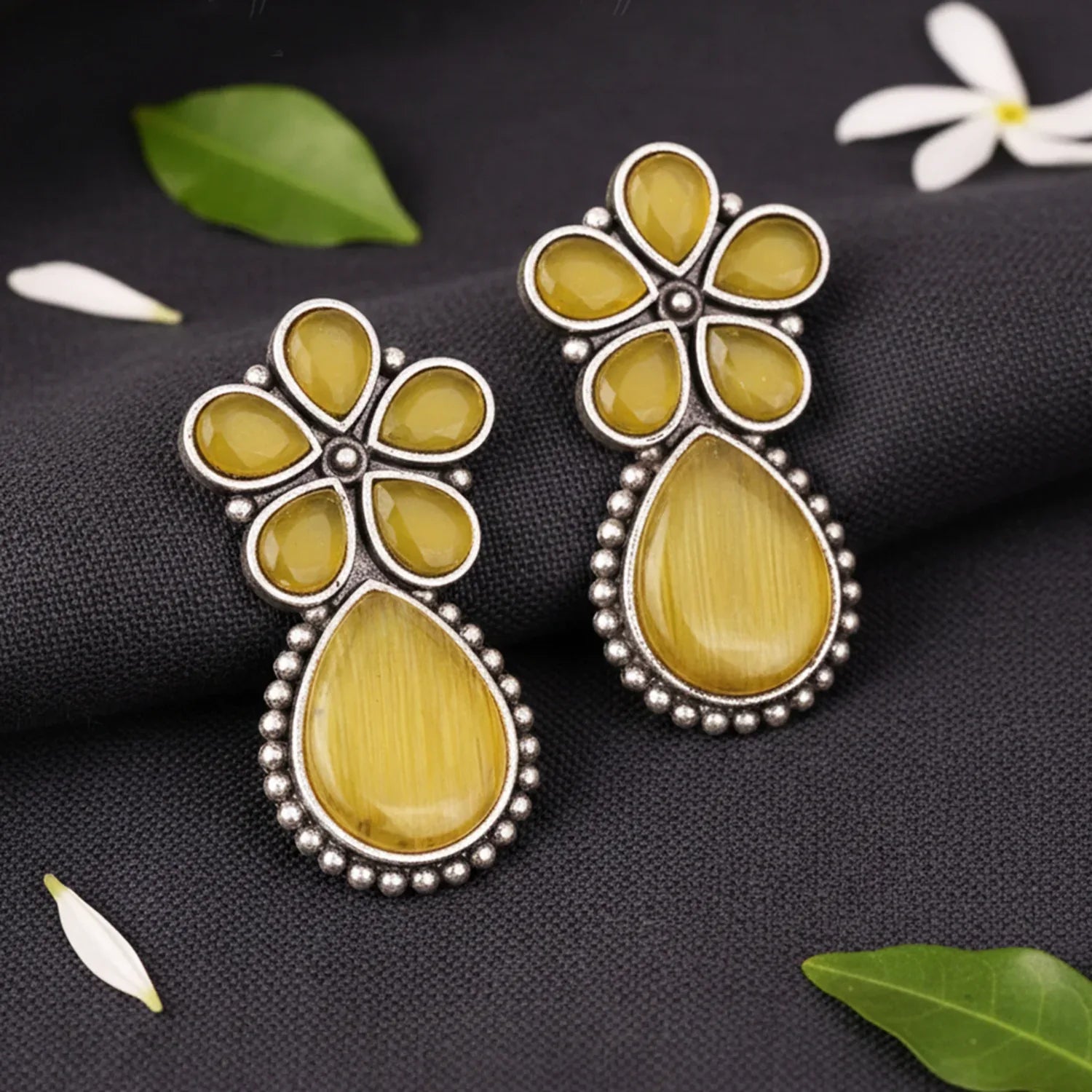 Pair of yellow floral earrings on a dark fabric background with leaves and flowers.