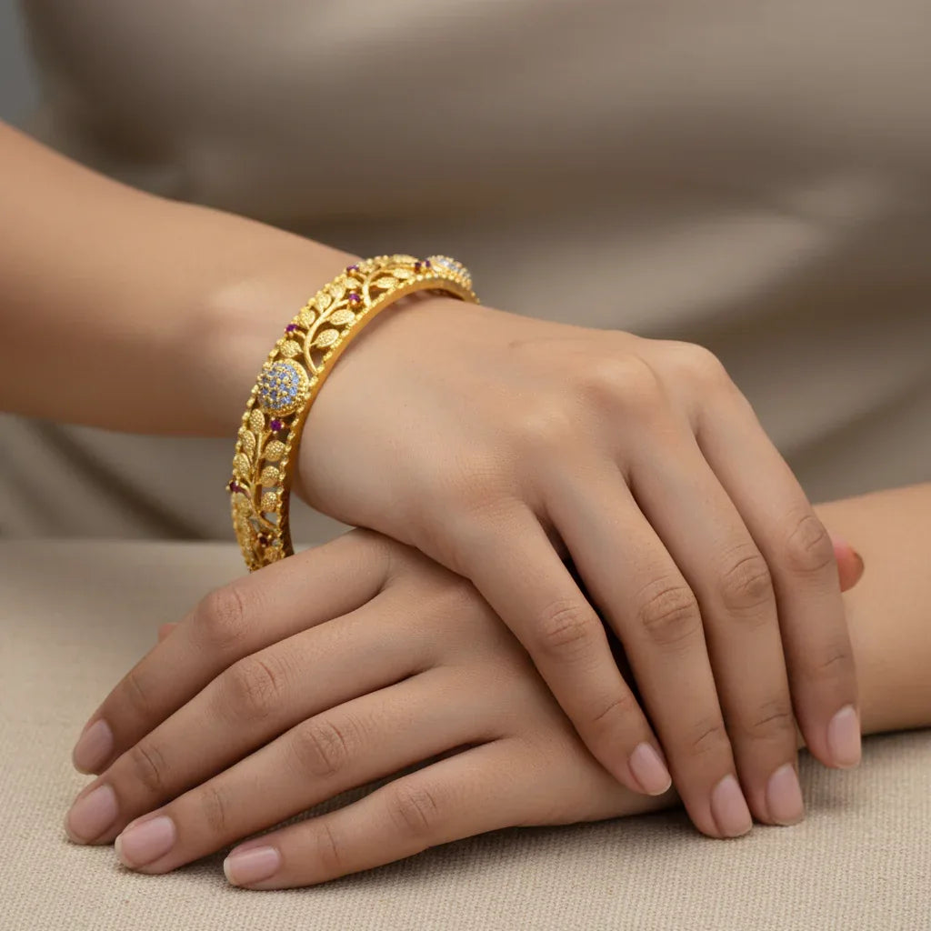 Gold bracelet with gemstones on a hand against a neutral background