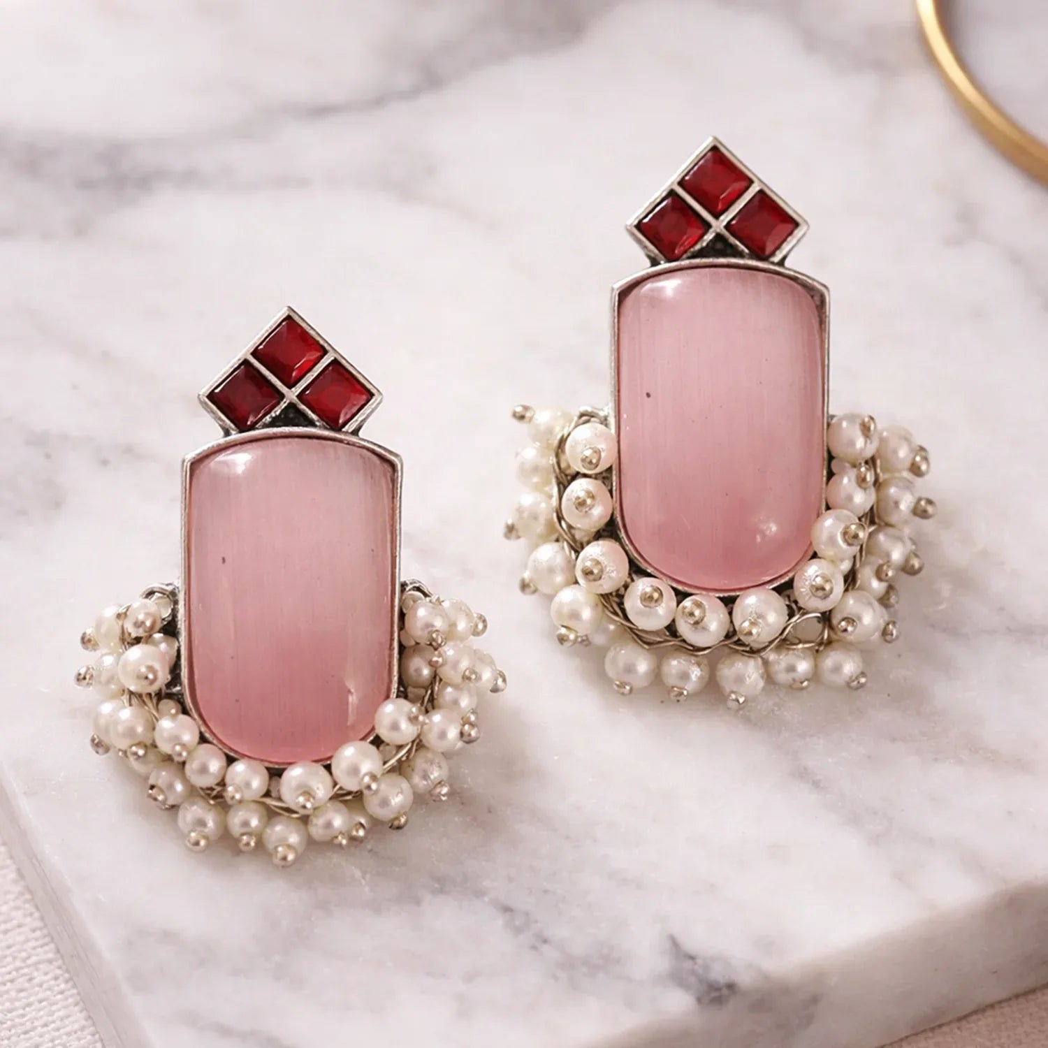 Pair of earrings with pink stones and pearl accents on a marble surface