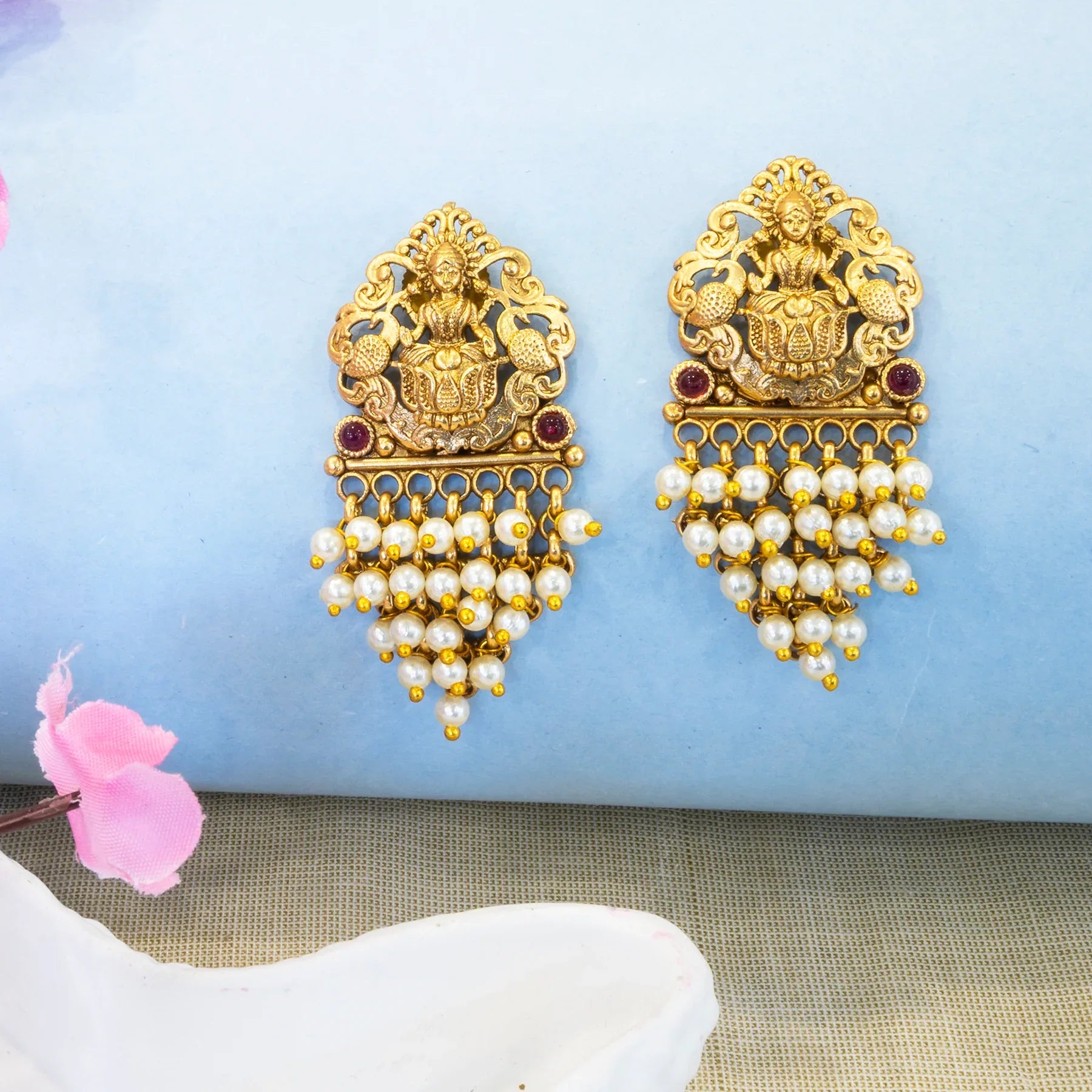 Gold earrings with pearl drops on a light blue fabric background