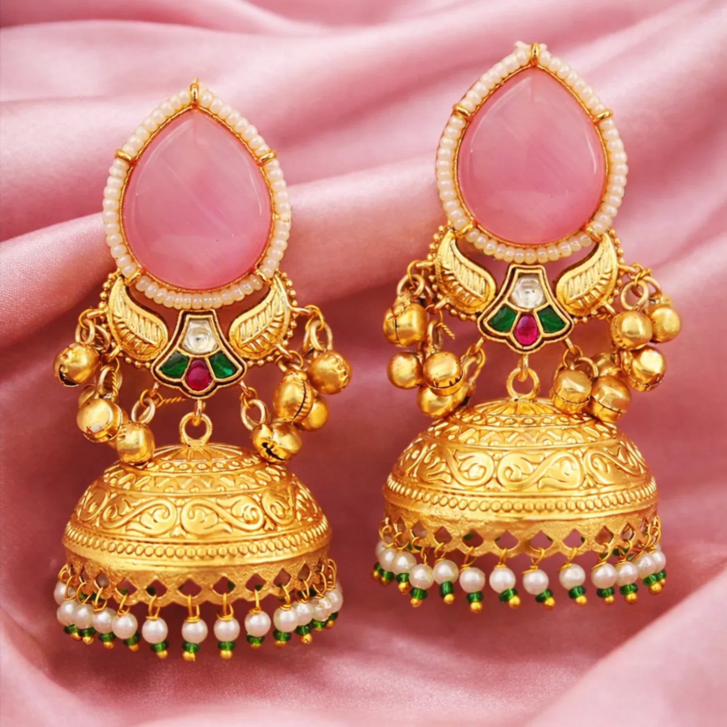 Gold earrings with intricate designs on a pink fabric background