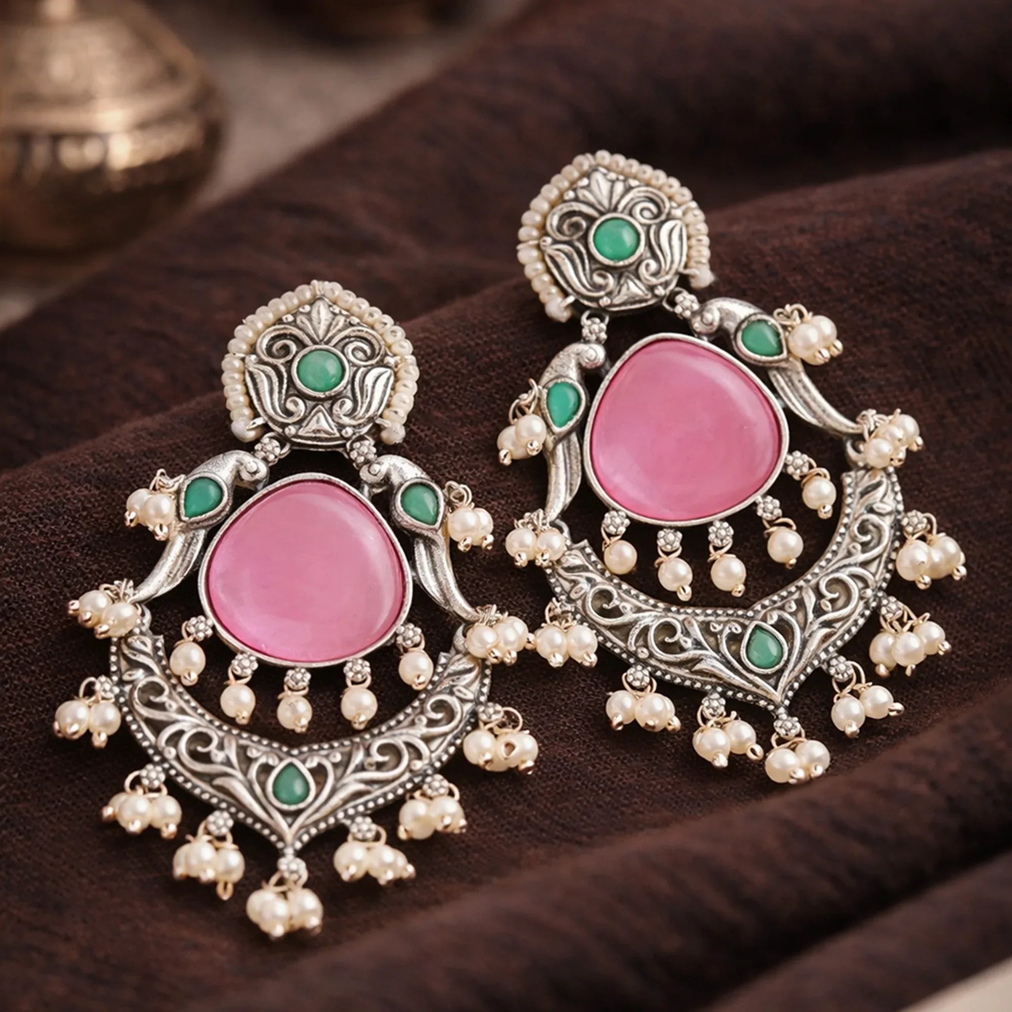 Ornate earrings with pink stones and pearl-like elements on a dark surface