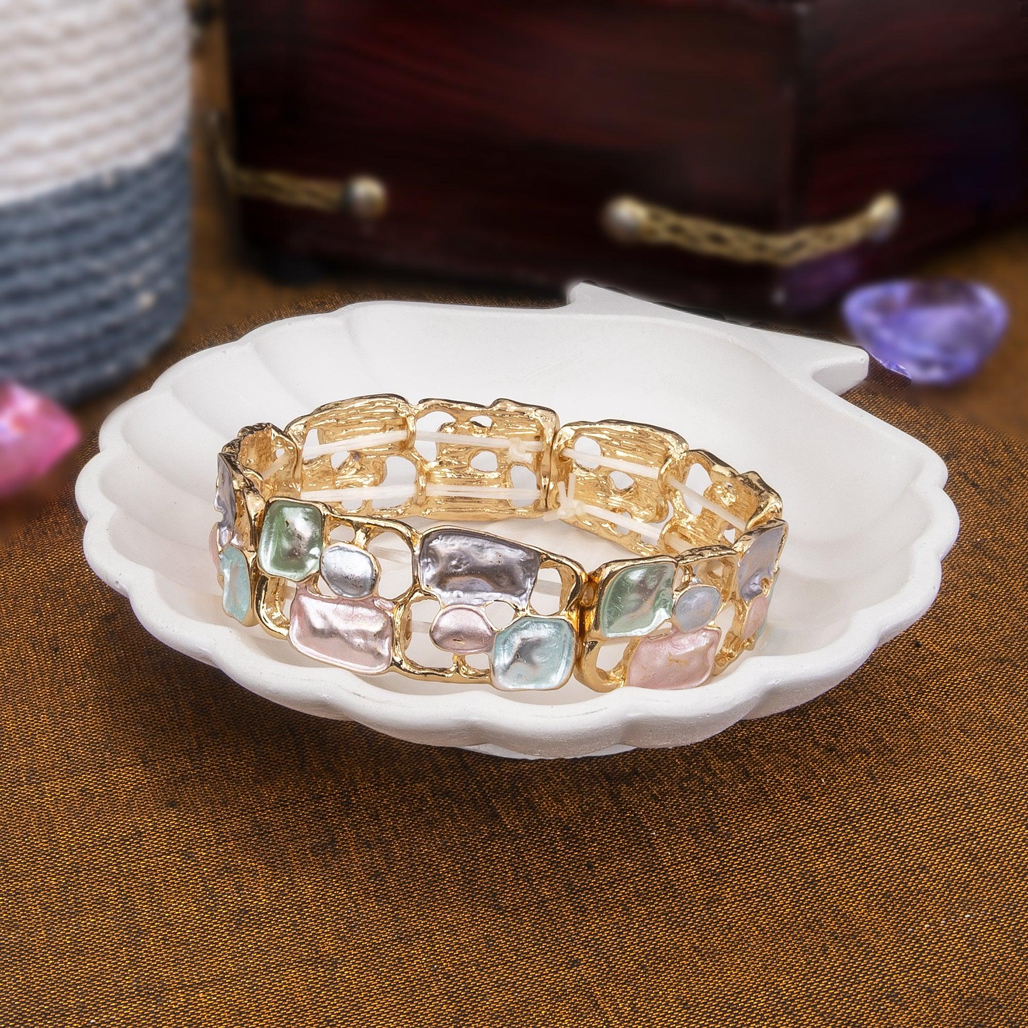 Gold bracelet with colorful stones on a white dish against a brown background