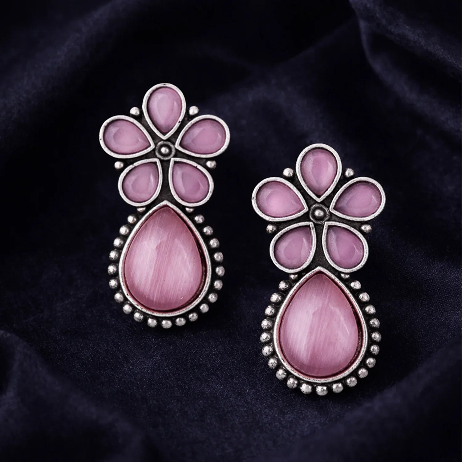 Pair of pink floral earrings on a dark fabric background