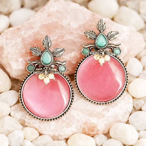 Pink earrings with green gemstones on a stone background