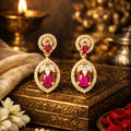 Gold earrings with red gemstones on a decorative box with flowers and candles in the background