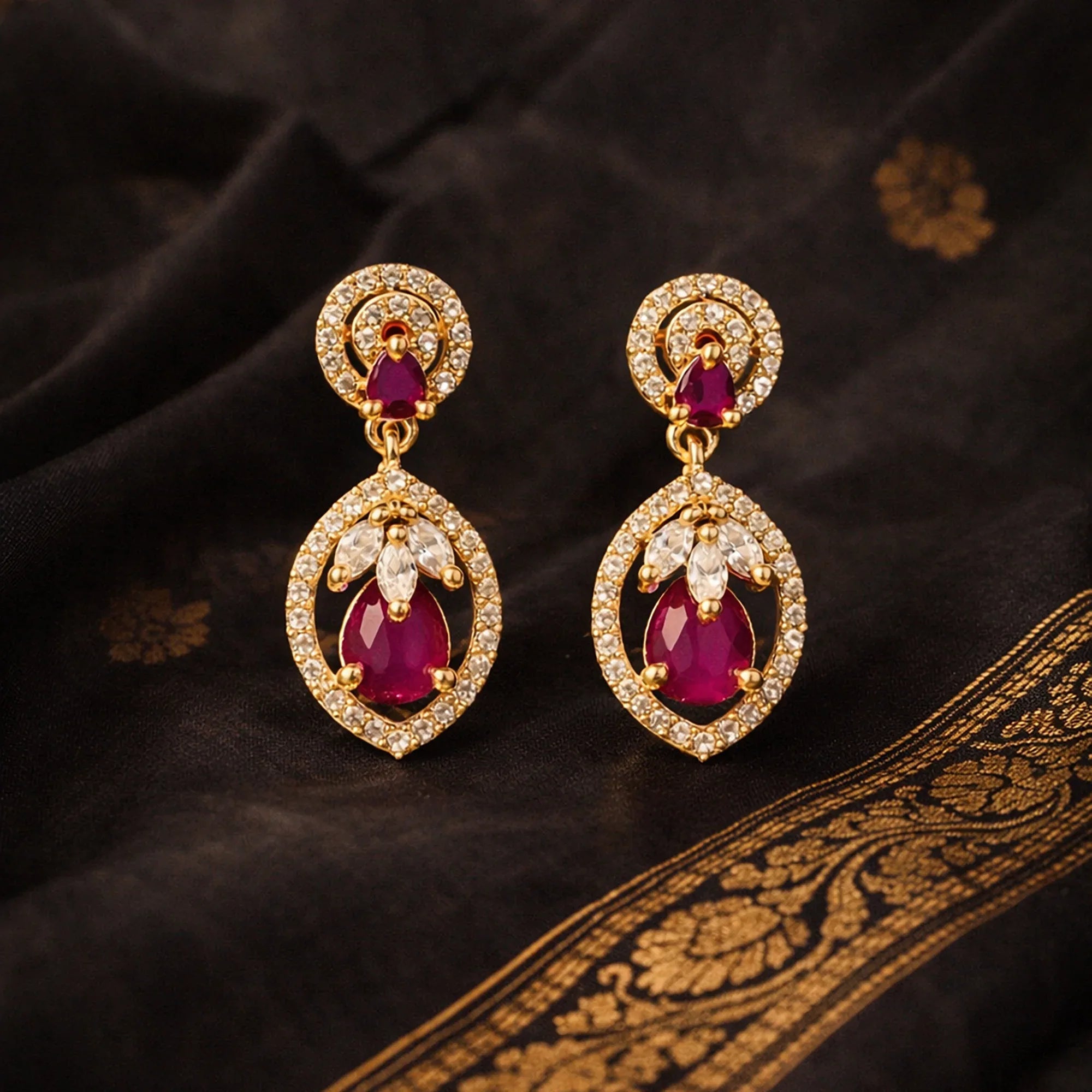 Gold earrings with red gemstones on a dark fabric background