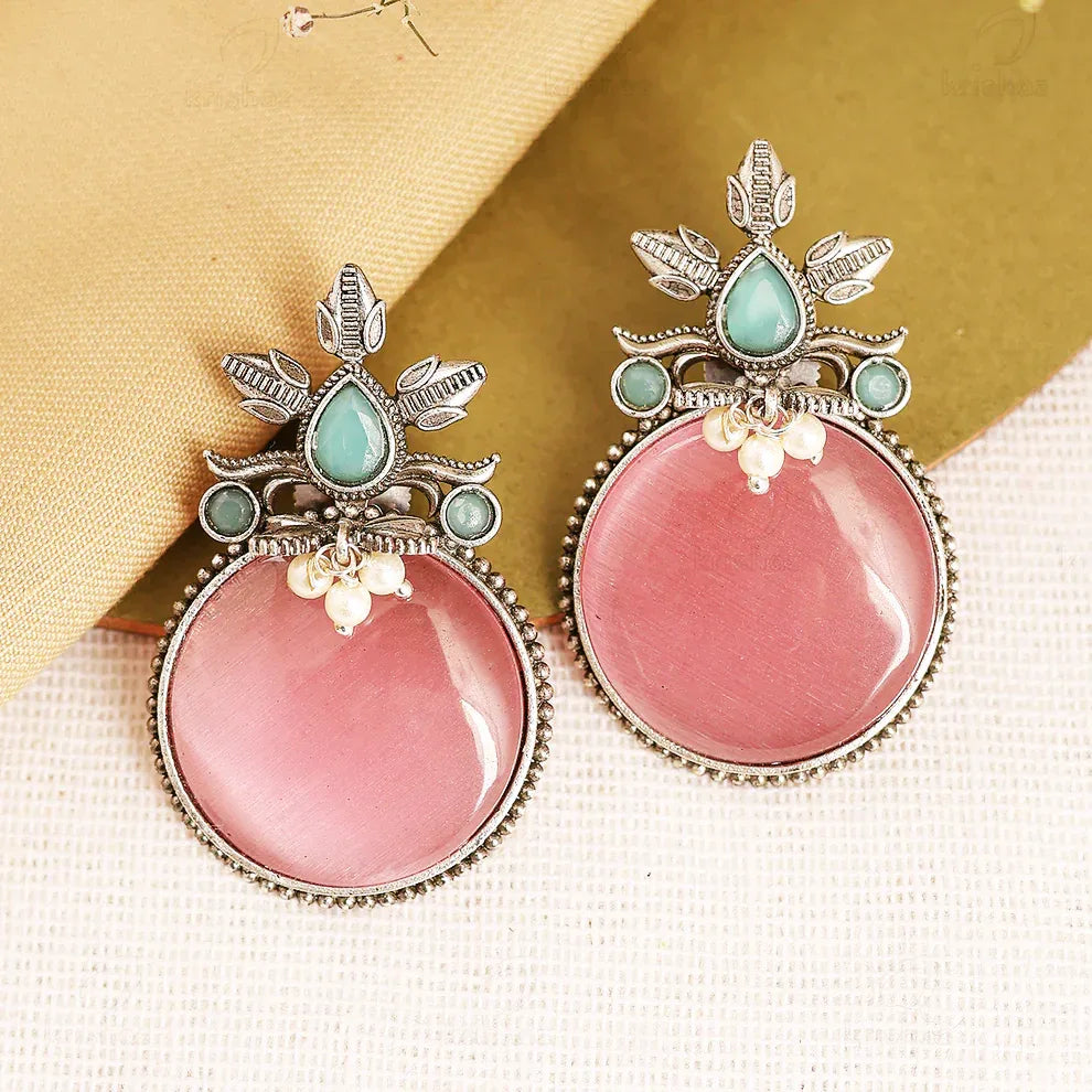 Pink earrings with silver and gemstone details on a textured surface