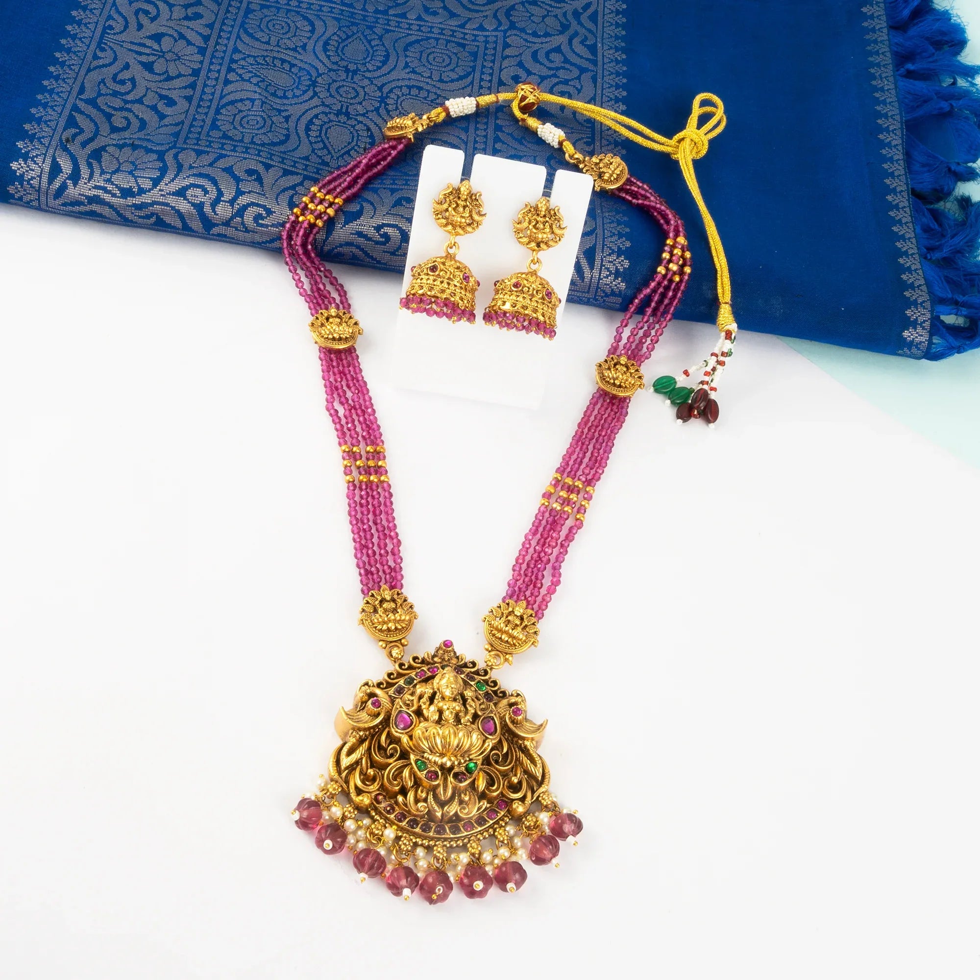 Gold necklace with pink beads and matching earrings on a white background
