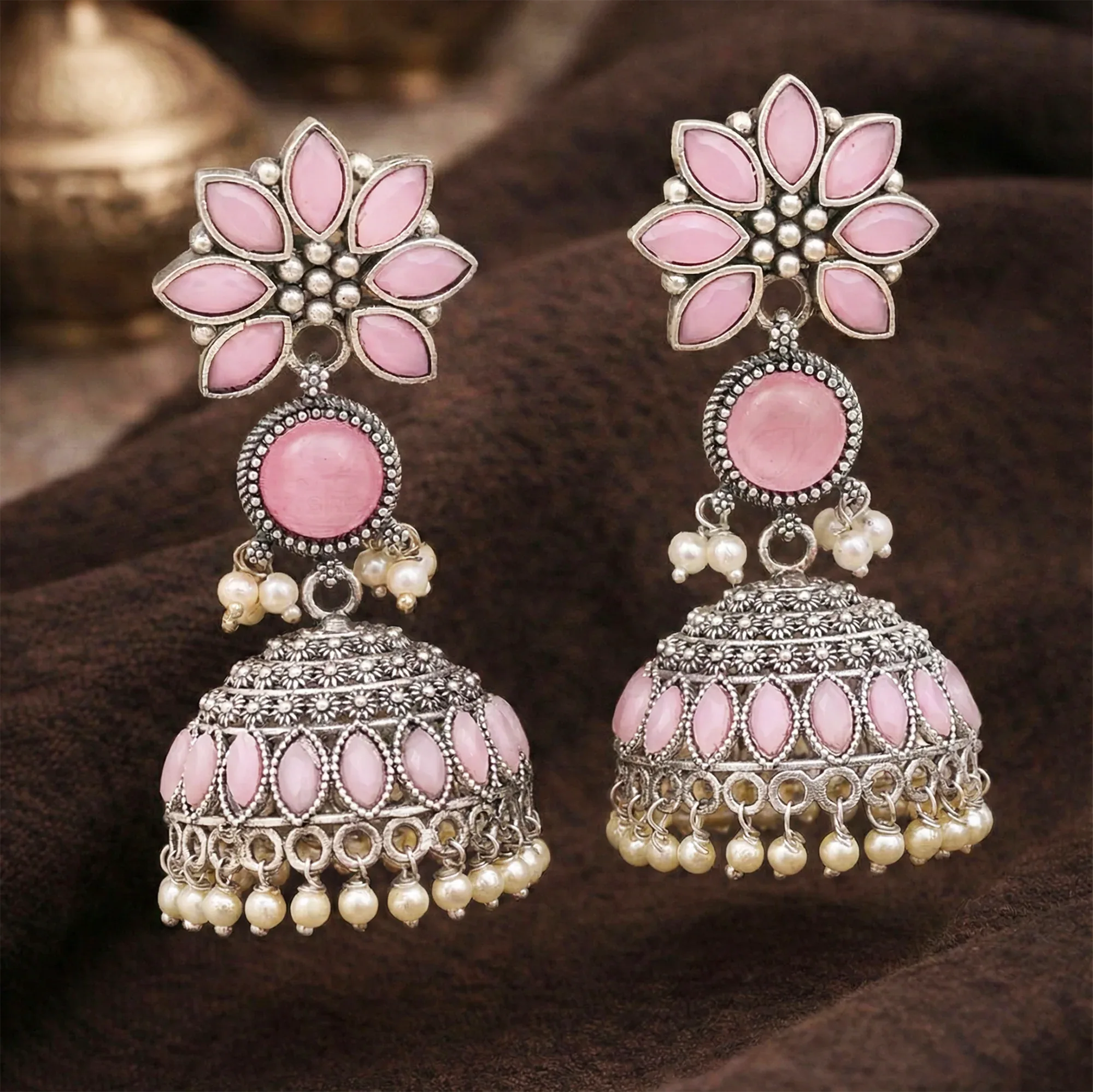 Pair of pink and silver earrings with floral designs on a brown background