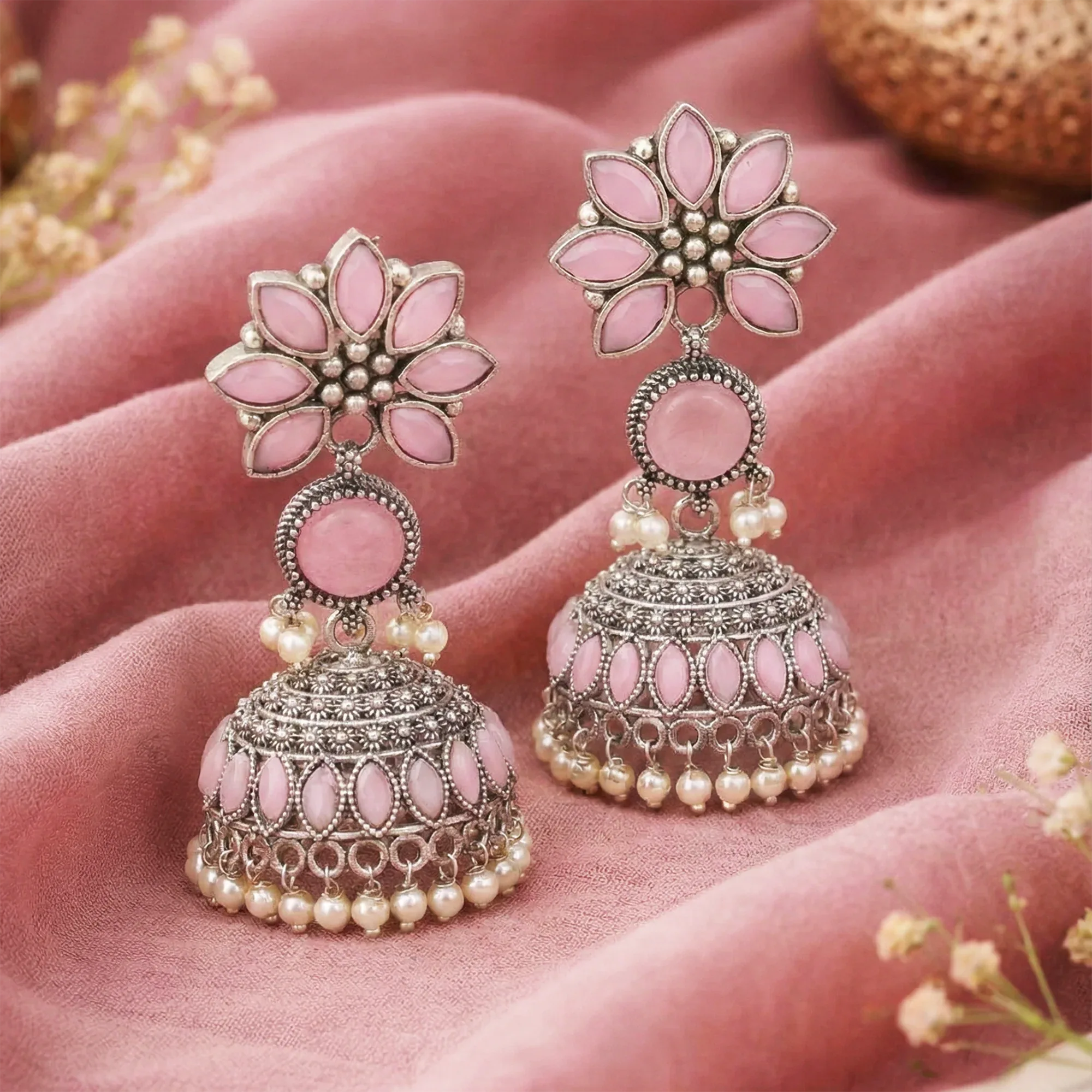 Pink floral earrings with silver and pearl details on a pink fabric background